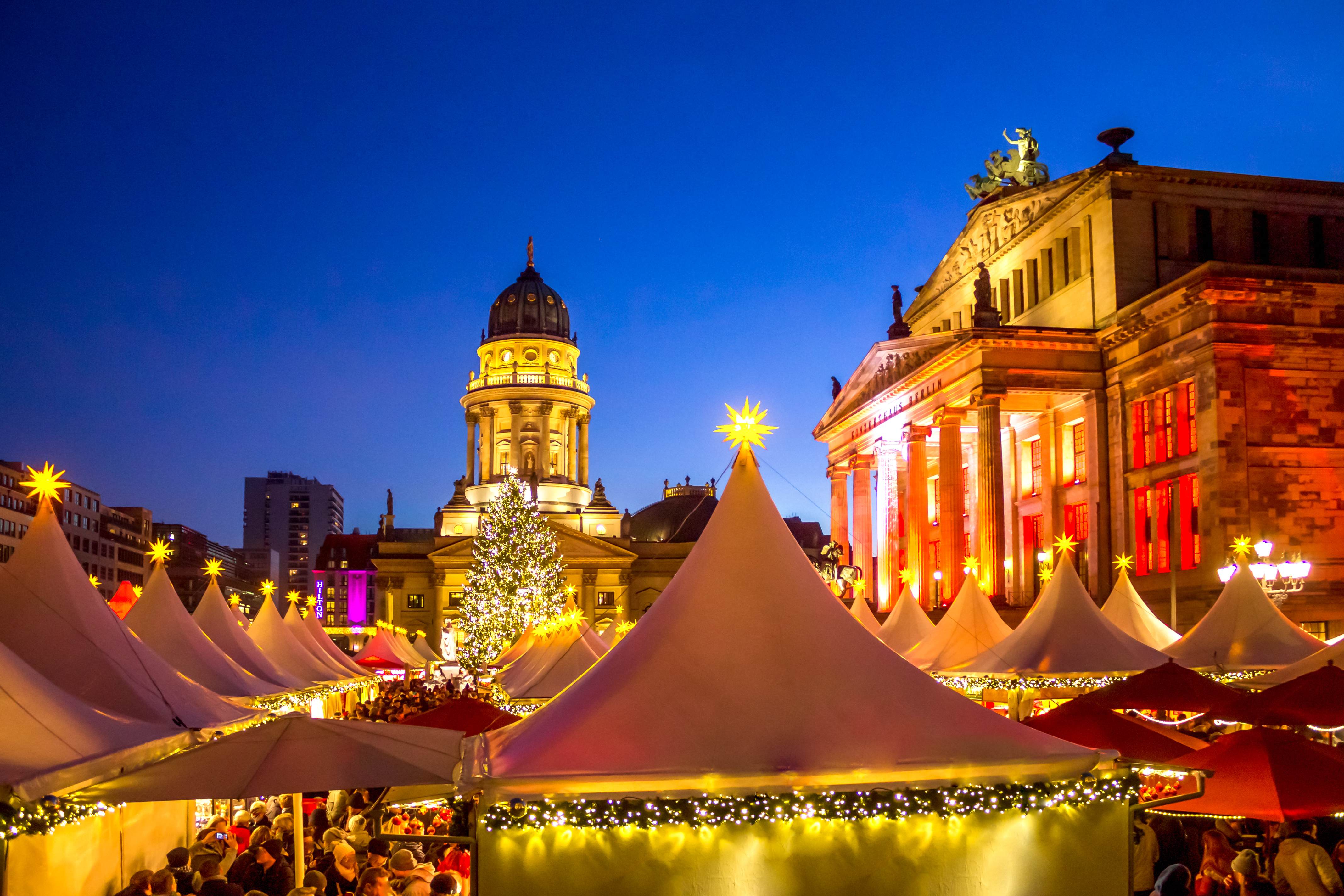Festligt julemarked på Gendarmenmarkt i Berlin med oplyste boder, juletræ og historiske bygninger mod den blå aftenhimmel