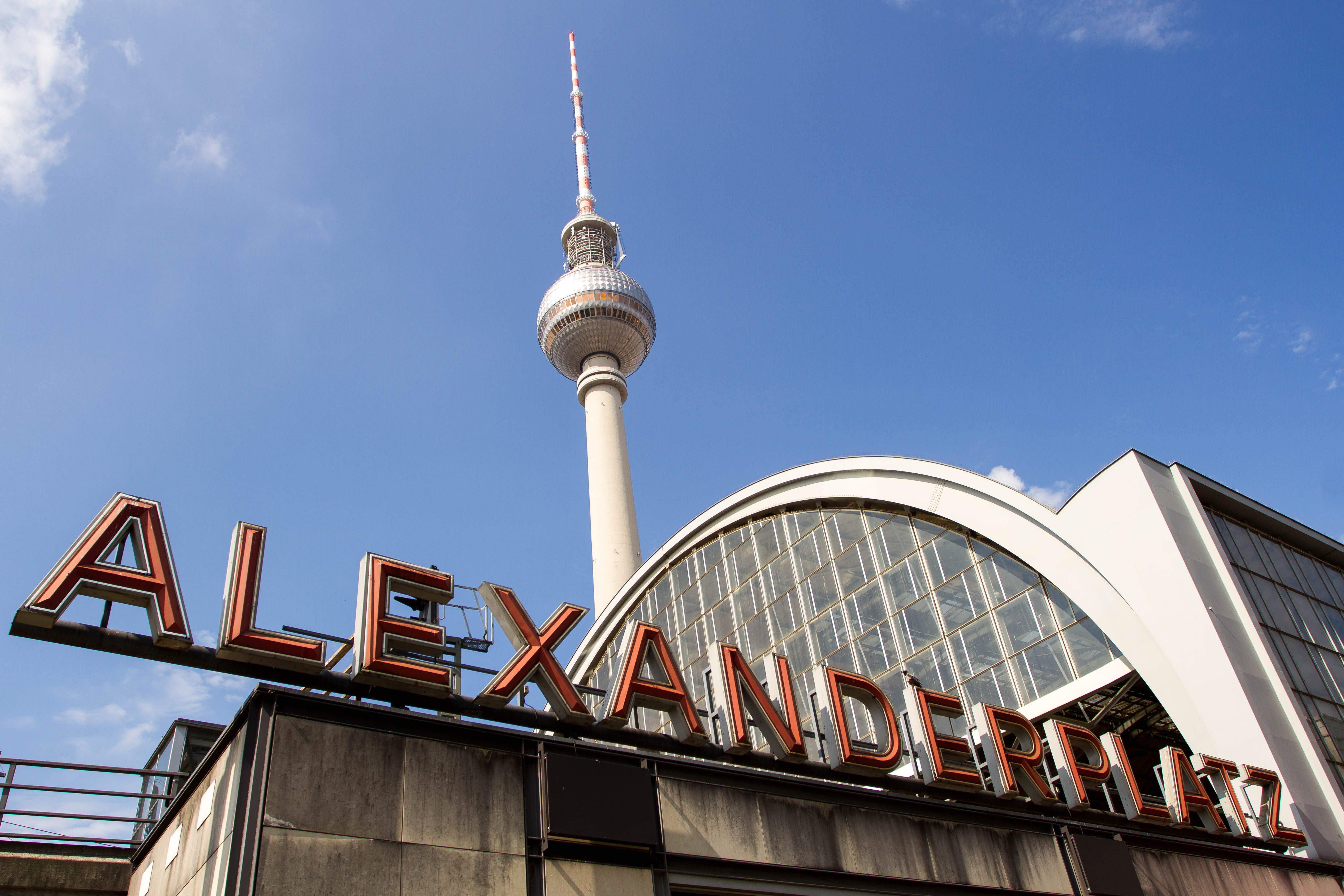 Berlins ikoniske TV-tårn Fernsehturm ses bag Alexanderplatz stationens hvælvede glasfacade og skiltet