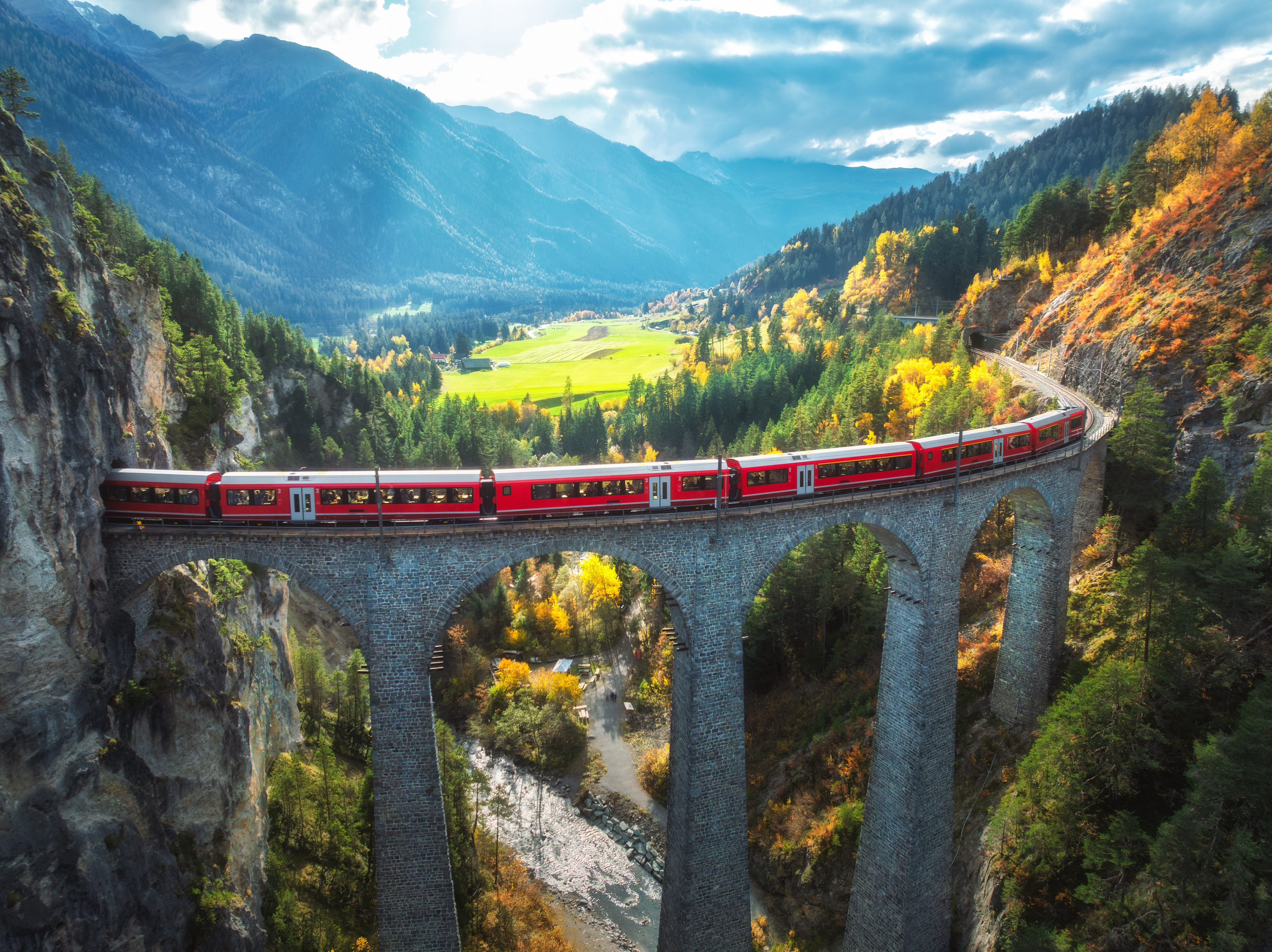 Fascinerende fugleperspektiv af det ikoniske røde Bernina Express tog på Landwasser Viadukten i Schweiz, med de majestætiske alper og flammende efterårsskove i baggrunden