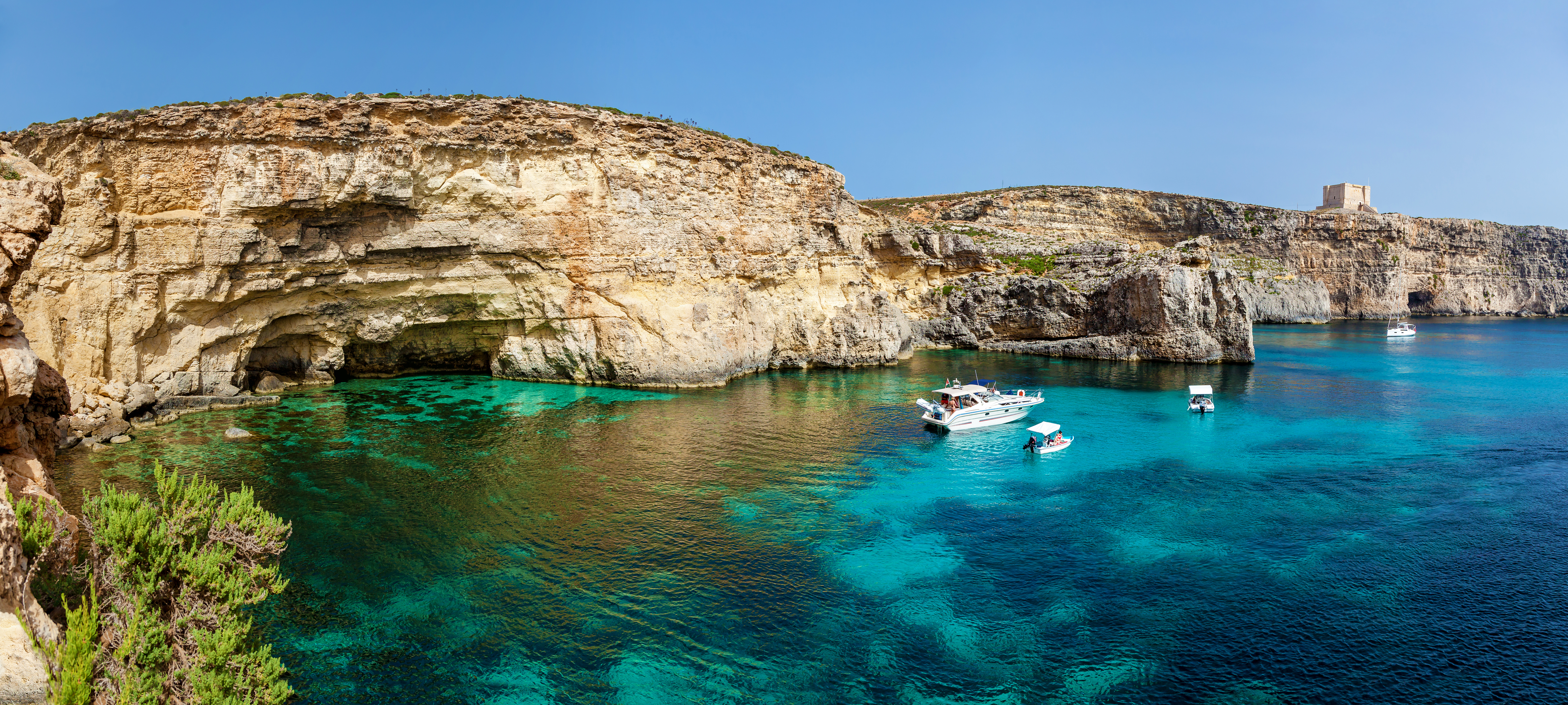 Det turkisblå vand i Comintos Blå Lagune i Malta med hvide både og imponerende kalkstensklipper – et populært rejsemål i Middelhavet