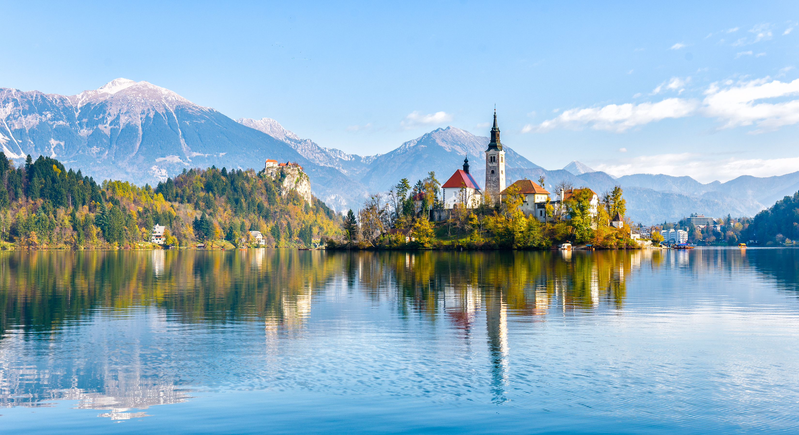 Idyllisk udsigt over Lake Bled i Slovenien med den karakteristiske økirke reflekteret i det spejlblanke vand og de julianske alper i baggrunden