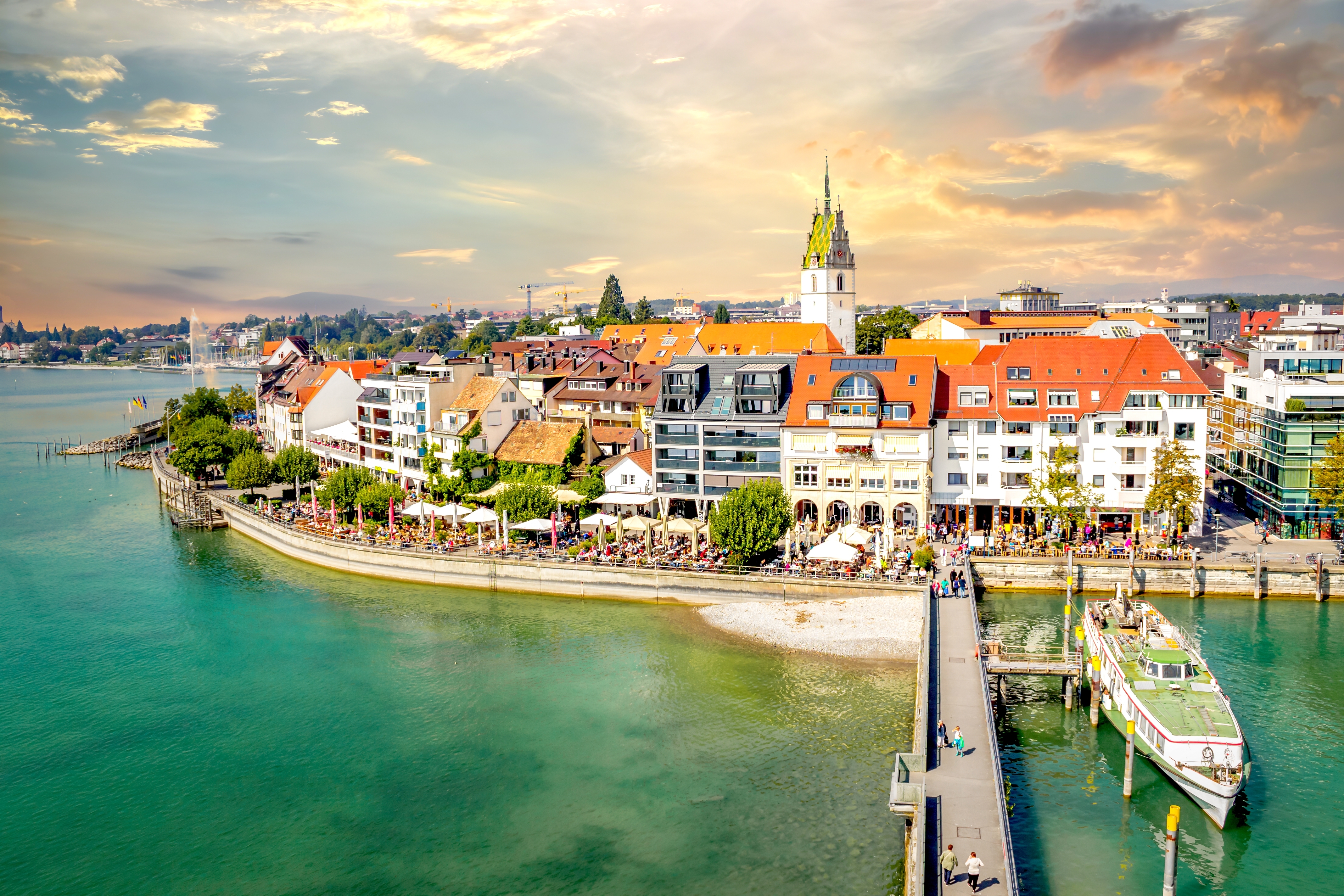 Udsigt over den historiske havn i Friedrichshafen ved Bodensøen med røde tage, kirkespir og turkisblåt vand