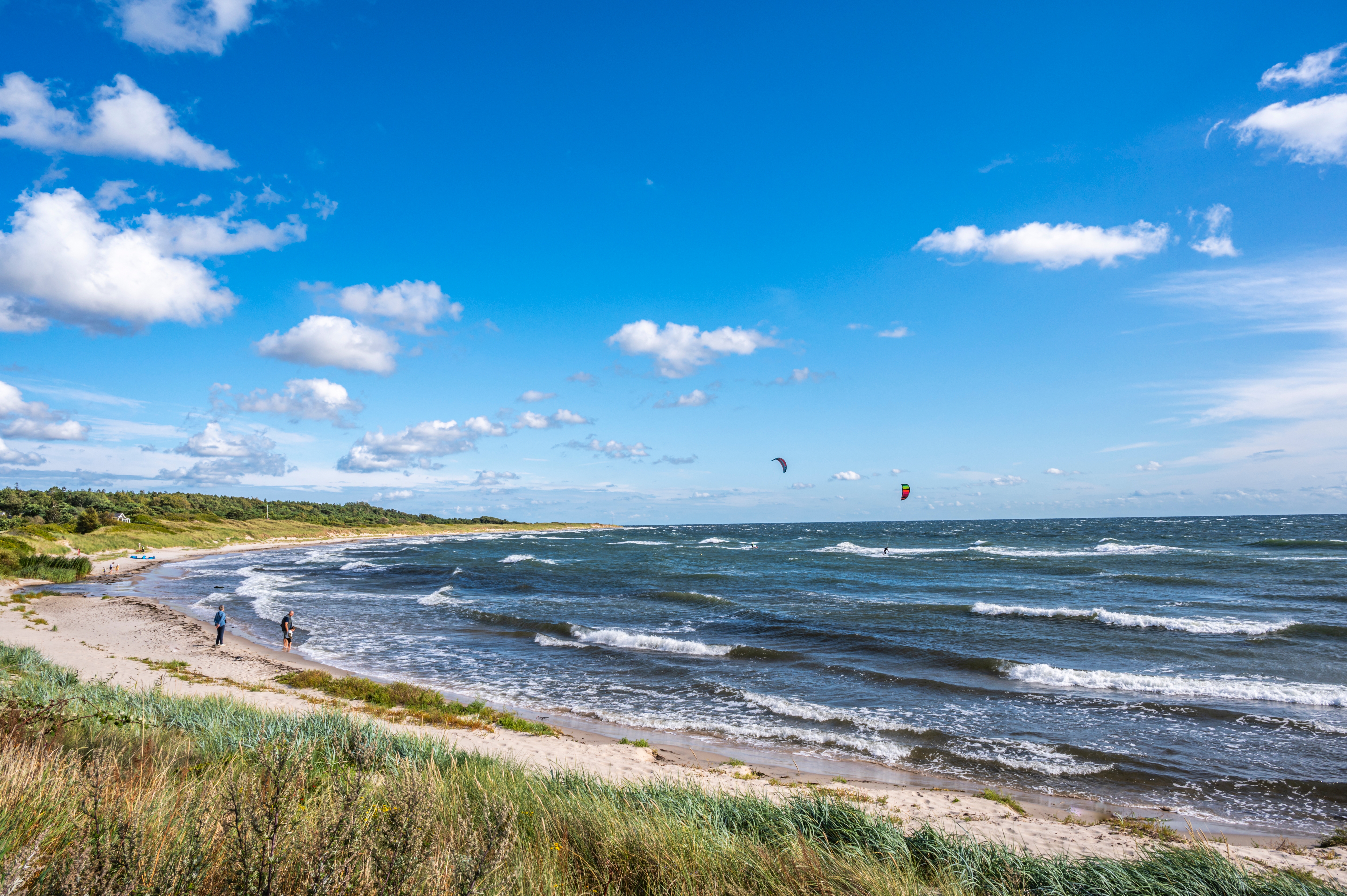 Afslappende strandudflugt ved Boderne på Bornholm med kitesurfere på Østersøen og en lys blå himmel med hvide skyer