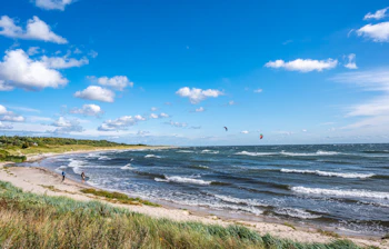 Afslappende strandudflugt ved Boderne på Bornholm med kitesurfere på Østersøen og en lys blå himmel med hvide skyer