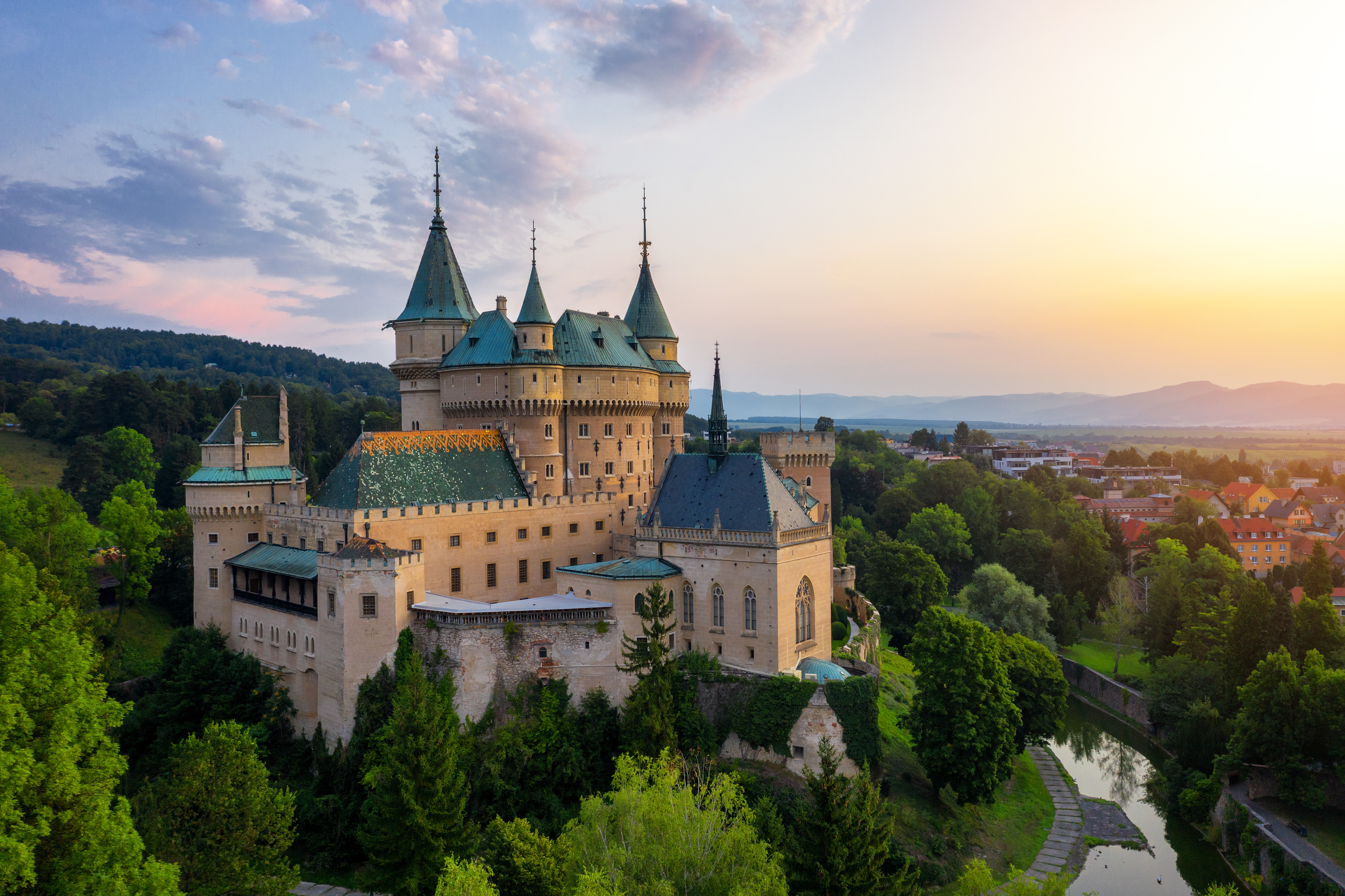 Smukt luftfoto af Bojnice Slot i Slovakiet ved solnedgang – et middelalderligt UNESCO-verdensarvssted med karakteristiske grønne tårne og frodig skovnatur