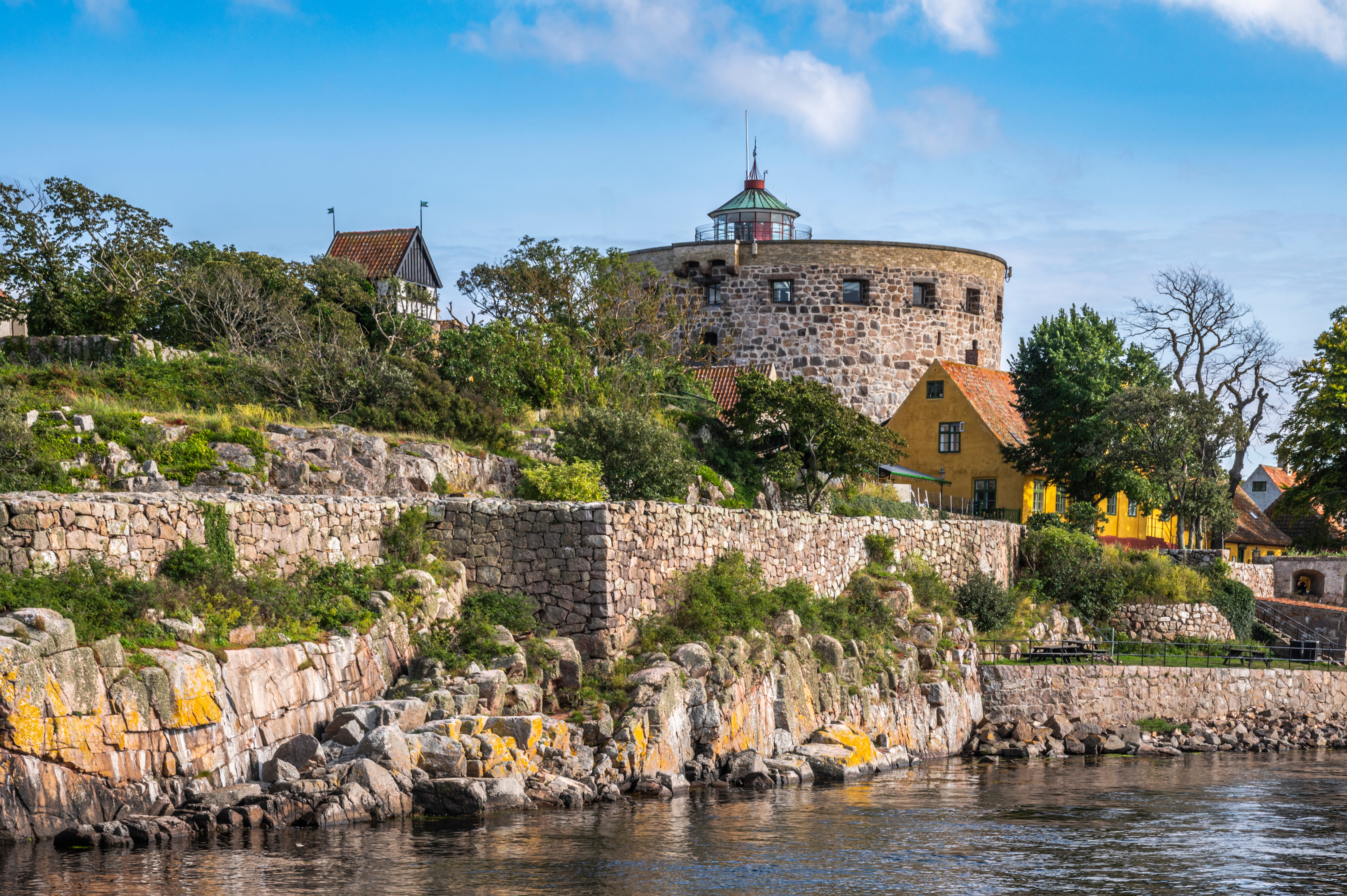 Historisk rundtårn på Christiansø nær Bornholm med stenbyggede mure langs kysten og smukke gule bygninger i sommersolskin