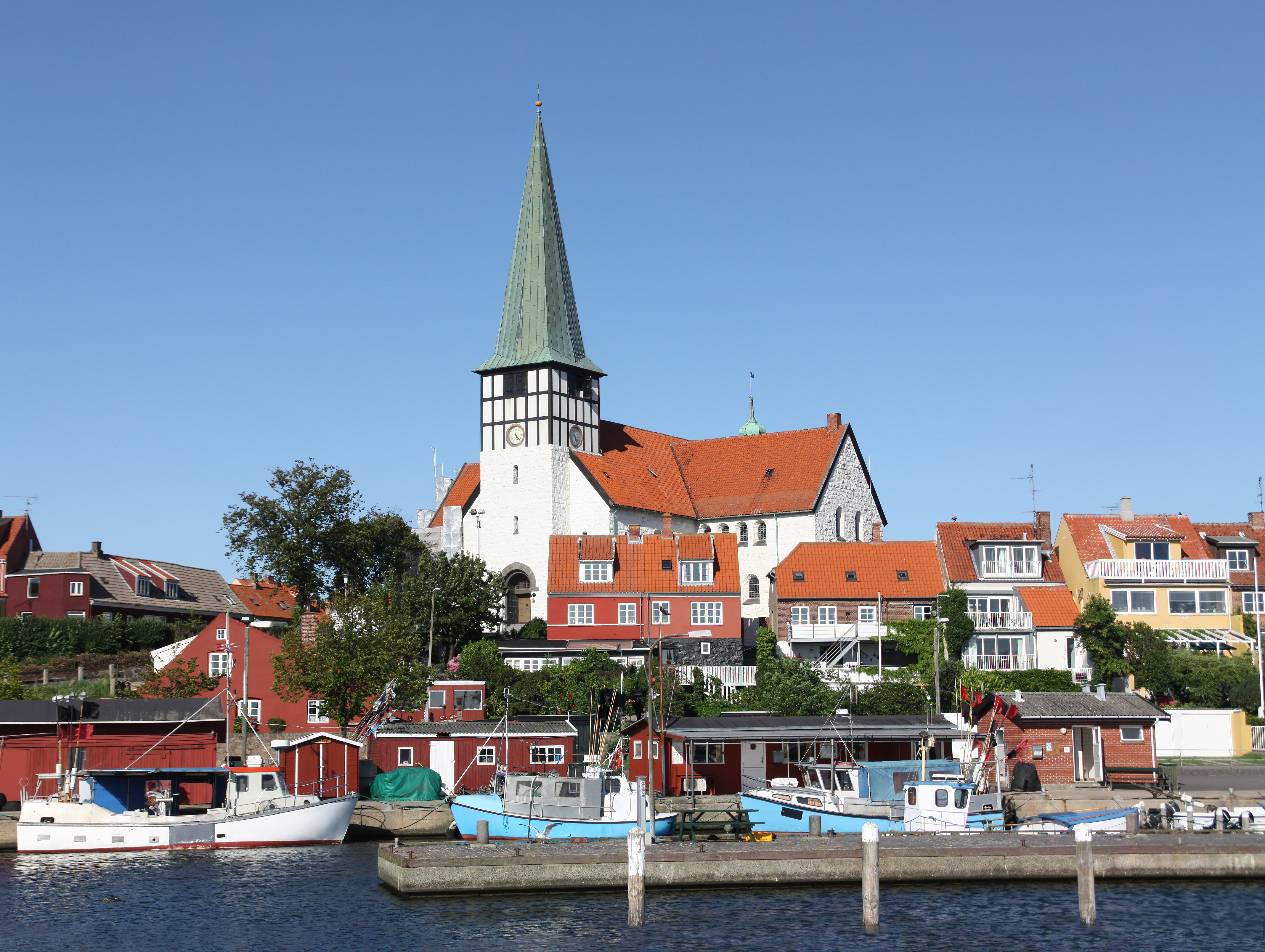 Stemningsfuld havn i Rønne på Bornholm med blå fiskerbåde og den ikoniske hvide kirke i baggrunden