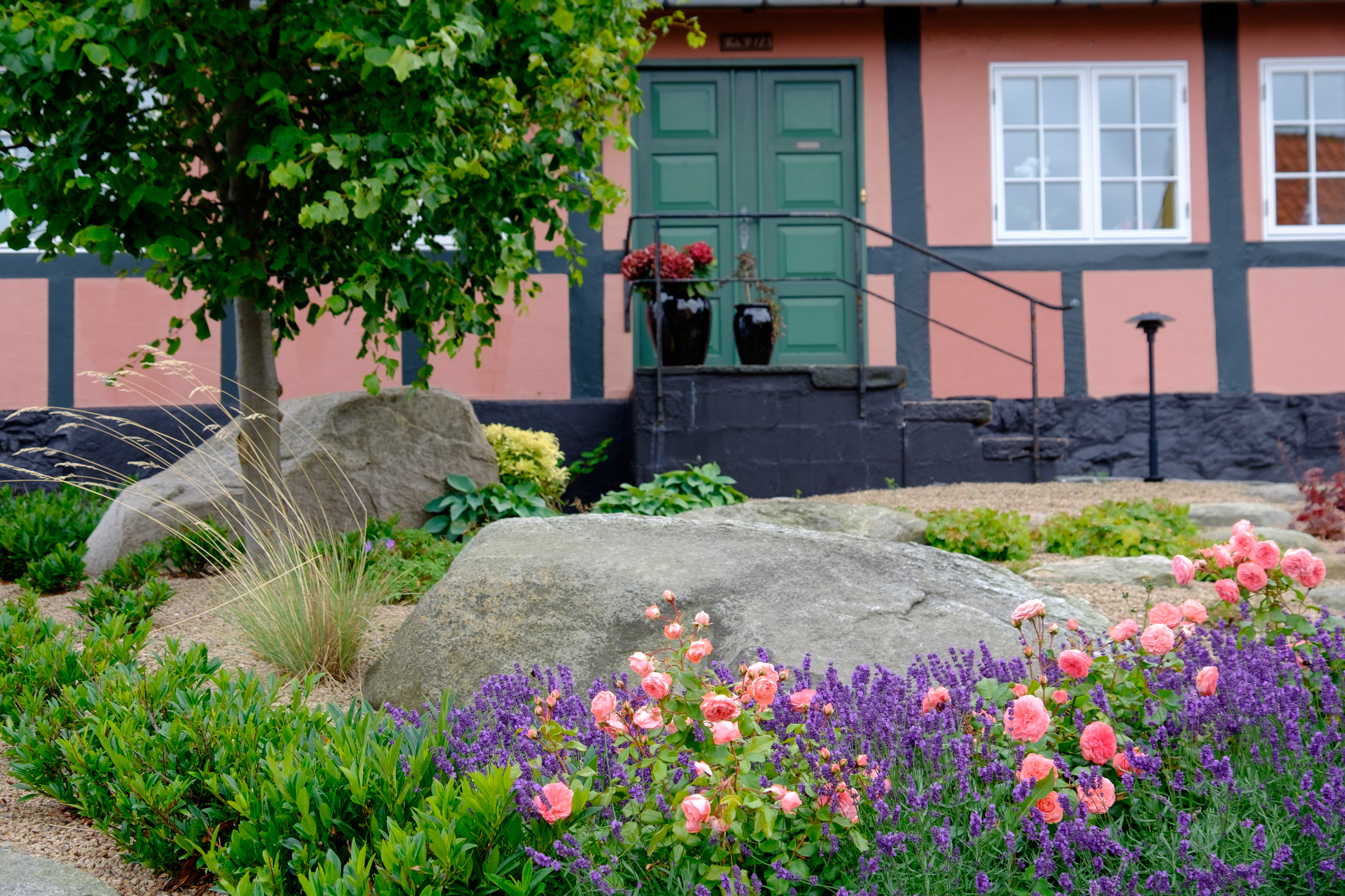 Smukt bindingsværkshus med grøn dør og farverig blomsterhave i Svaneke på Bornholm