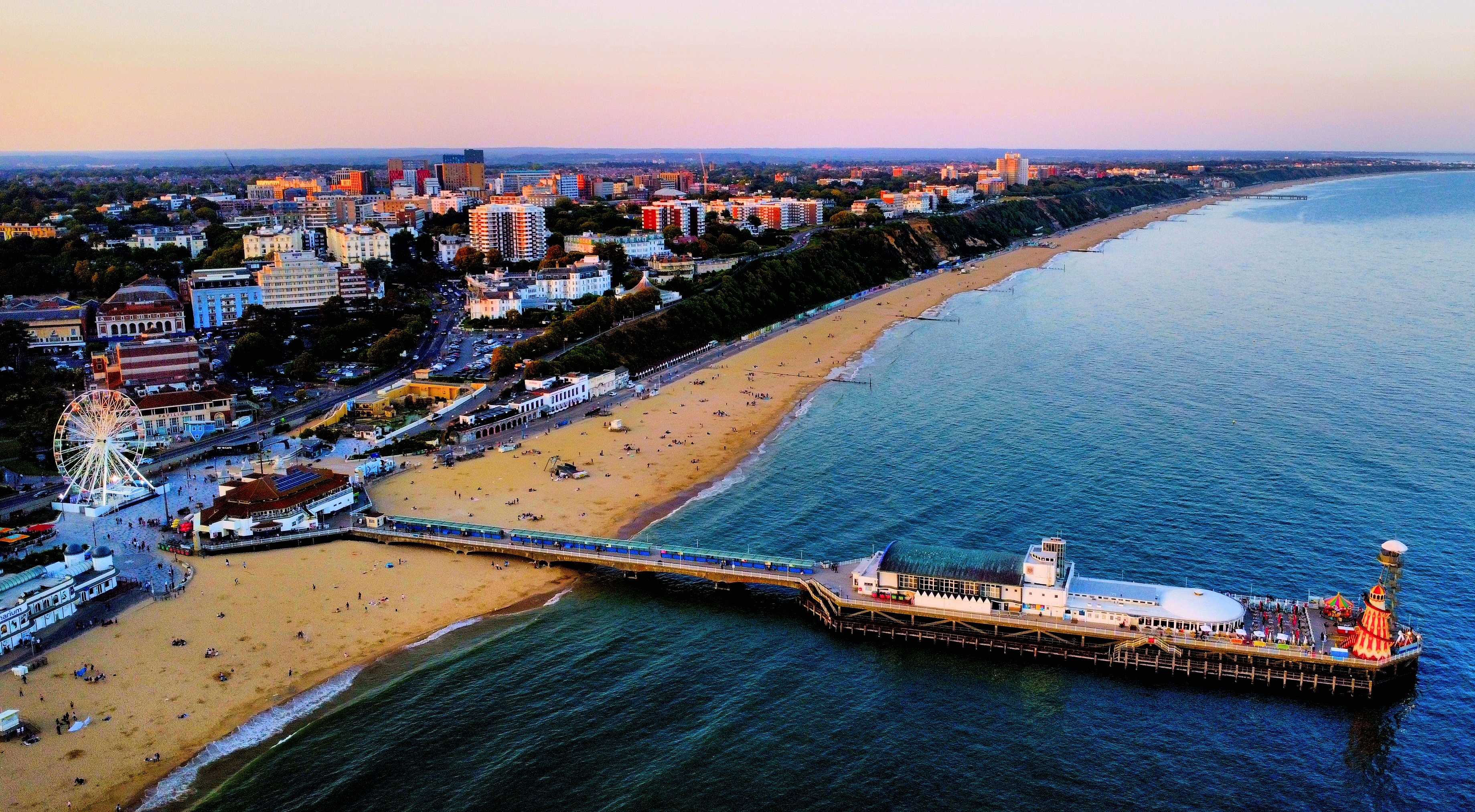 Luftfoto af Bournemouth med sandstrand, pier og pariserhjul badet i solnedgangens varme lys