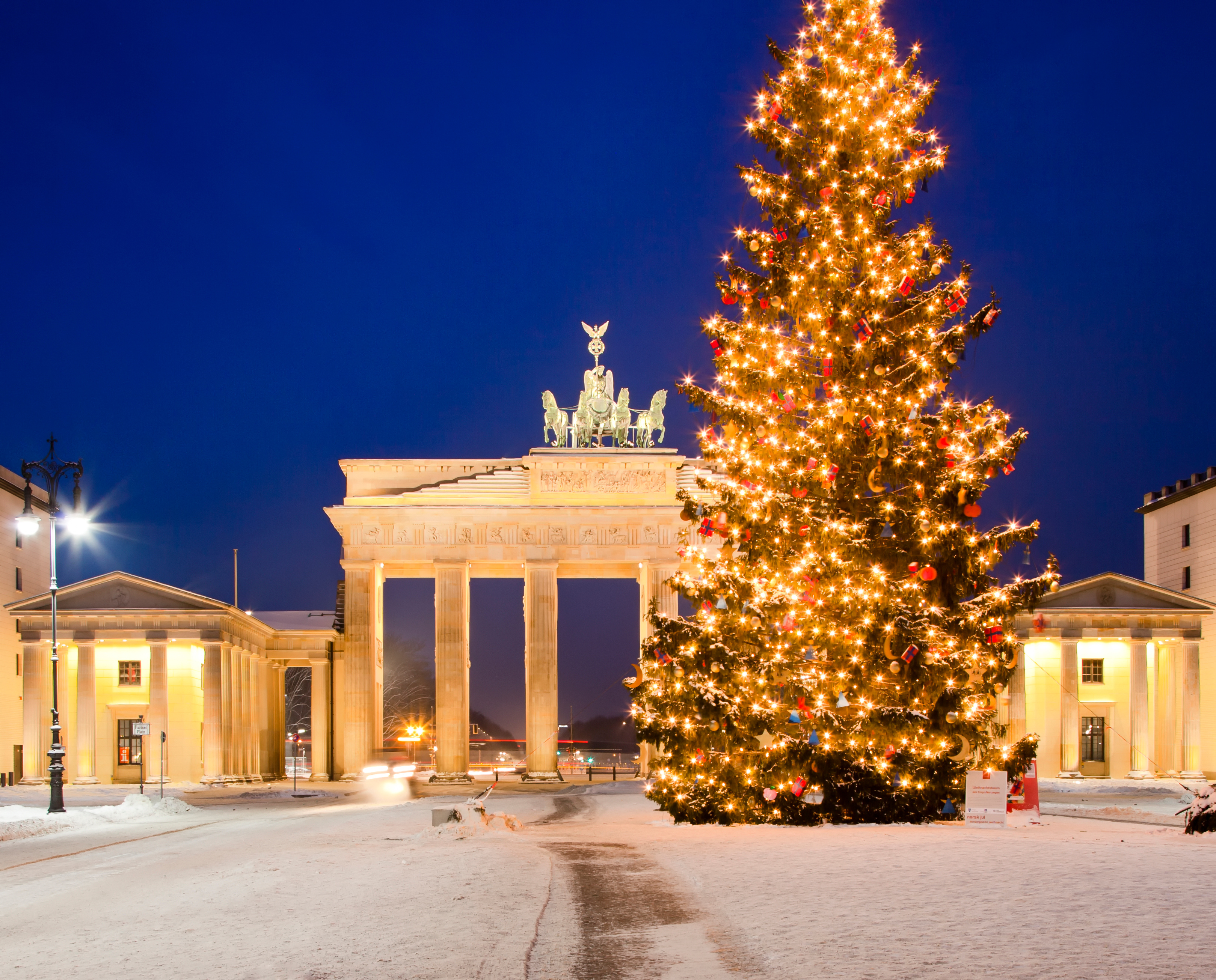 Julestemning ved Brandenburger Tor i Berlin med stort lysende juletræ og sne på gaden i adventstiden