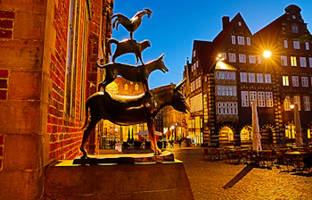 Bremer Bymusikanterne bronzestatue fotograferet ved aftentid med den historiske bykerne og bindingsværkshuse på markedspladsen i Bremen, Tyskland