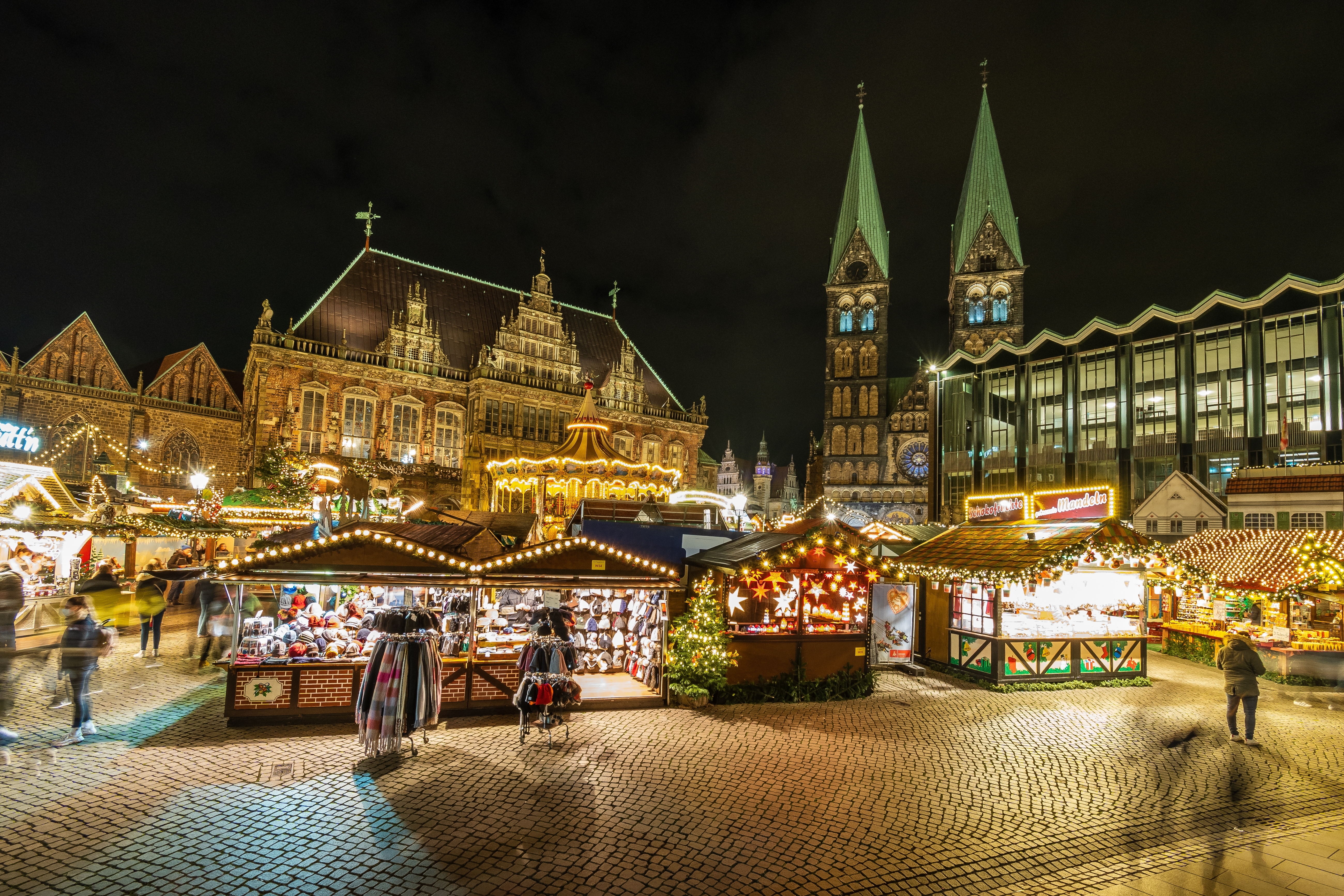 Julestemning på julemarkedet i Bremen med farverige boder, lysdekorationer og Bremer Dom i baggrunden en vinterfteraften