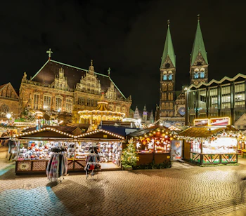 Julestemning på julemarkedet i Bremen med farverige boder, lysdekorationer og Bremer Dom i baggrunden en vinterfteraften