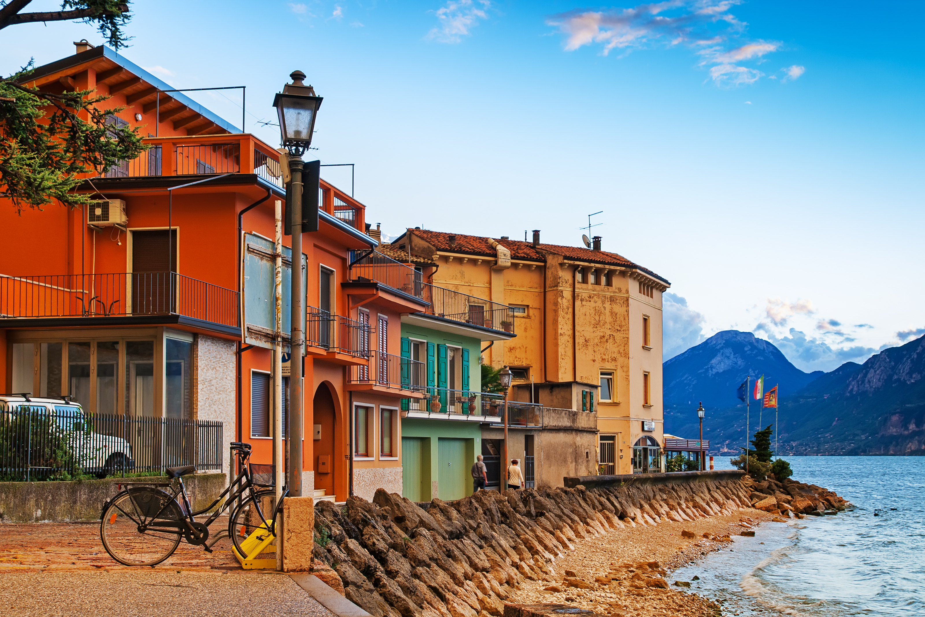 Smukke farverige huse langs Gardasøens bred i Brenzone sul Garda, Italien, med bjergtoppe og blå himmel i baggrunden