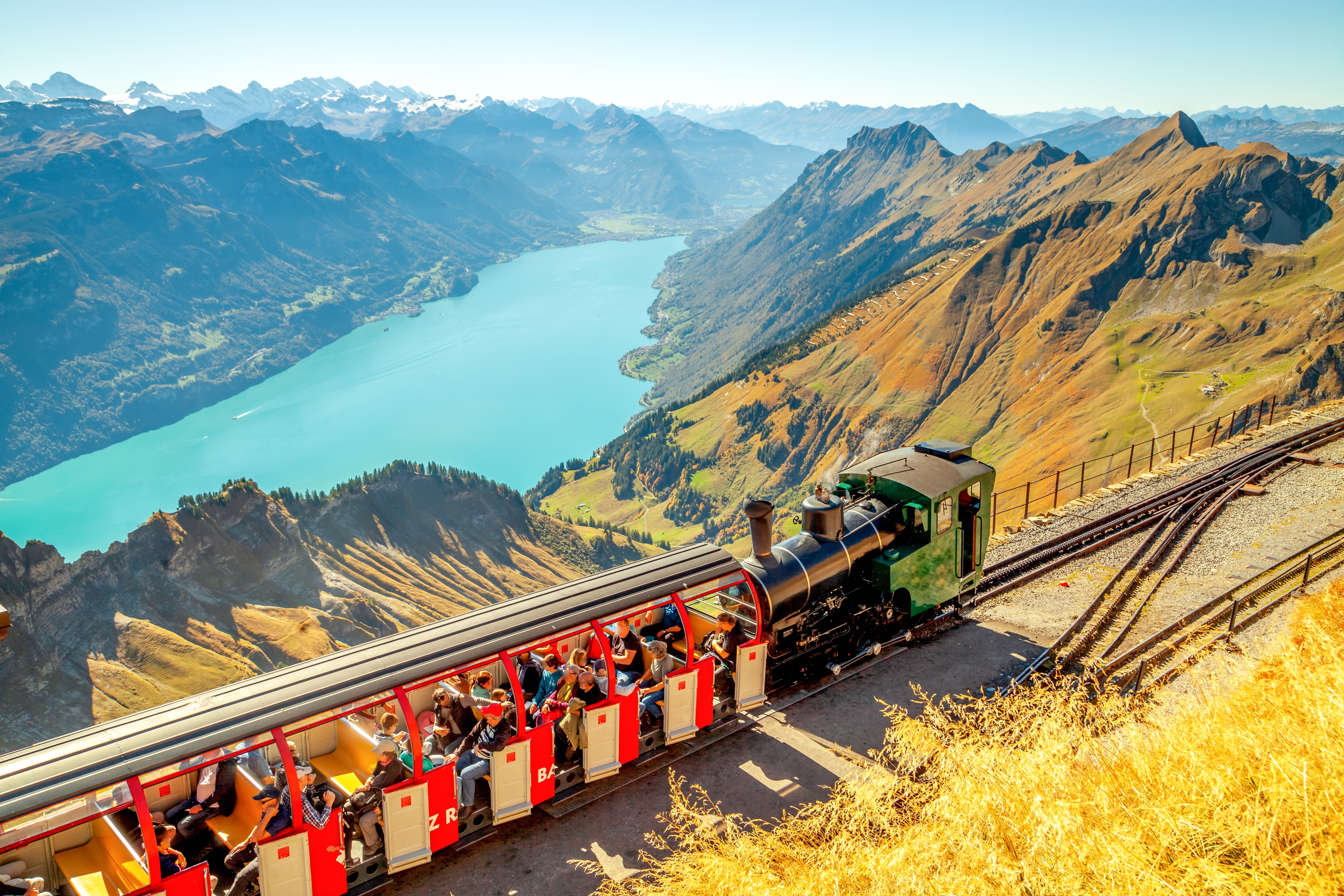 Passagerer nyder turen med Brienz Rothornbanen i Schweiz med storslået udsigt over Brienzersøen og de majestetiske alper
