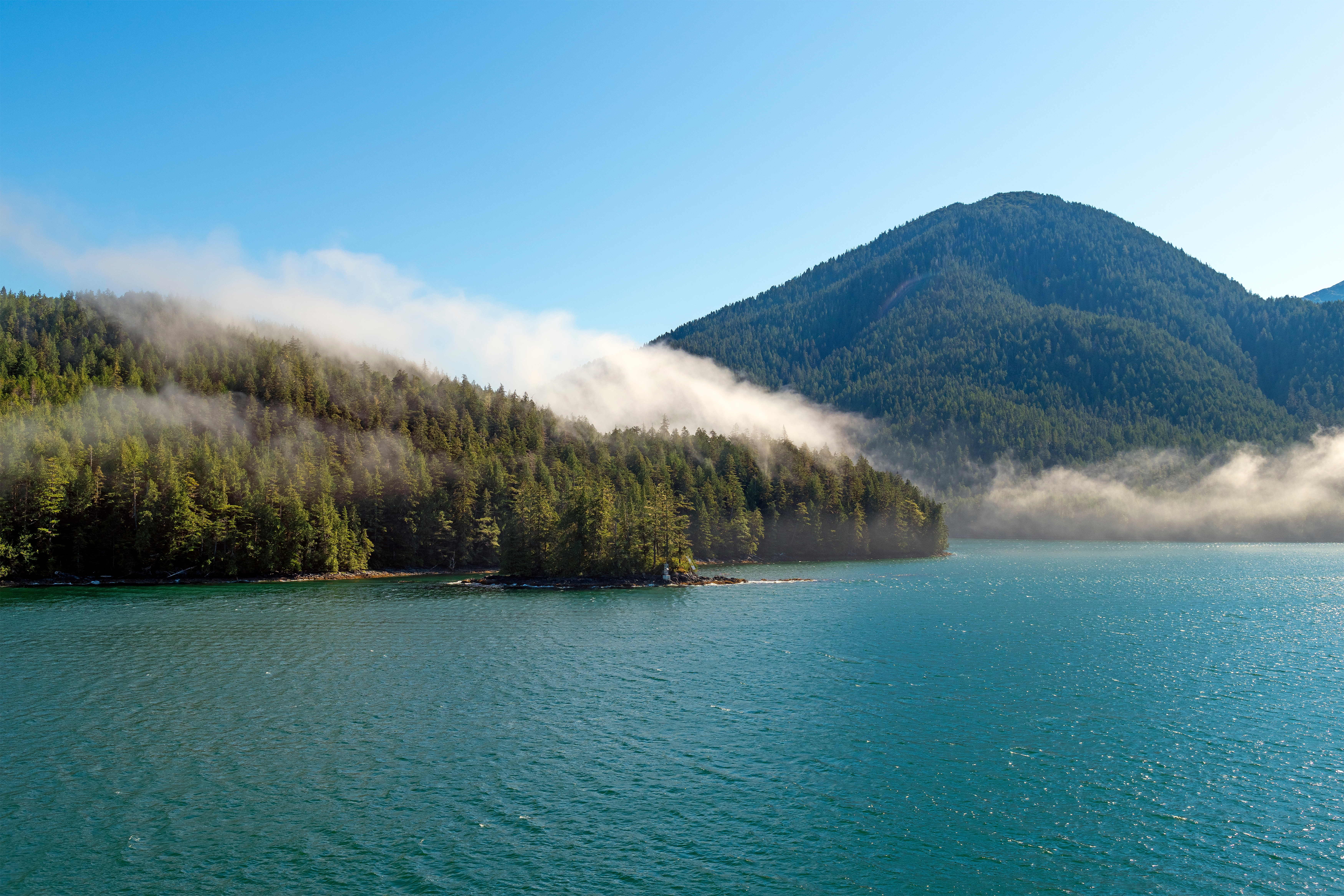 Naturskønt udsyn over det turkisfarvede hav med tåge der letter fra de skovklædte bjerge langs Inside Passage i British Columbia, Canada