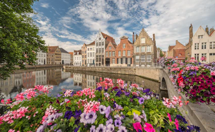 Charmerende kanal i Brügge med farverige blomster og traditionel flamsk arkitektur