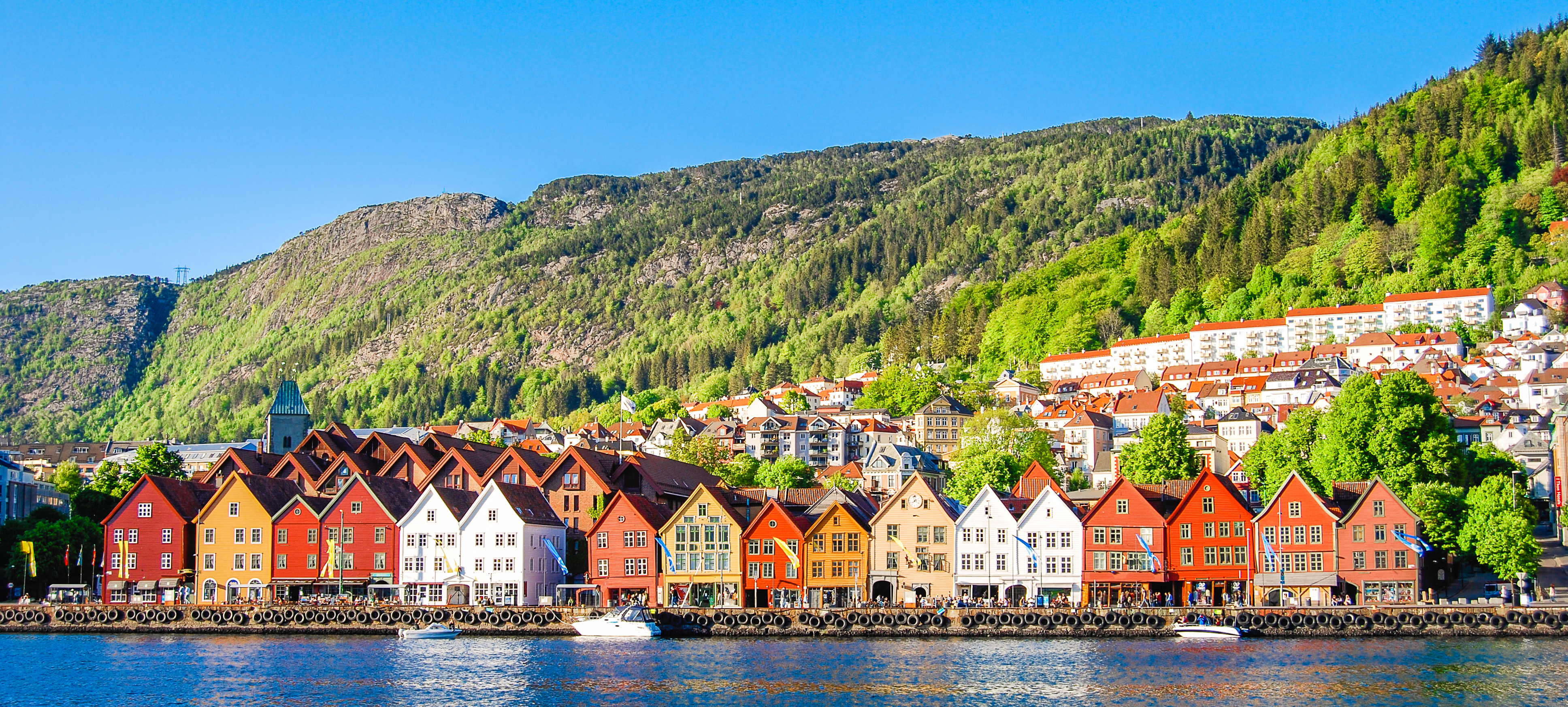 Historiske farverige huse ved Bryggen i Bergen omgivet af grønne bjerge og blå himmel