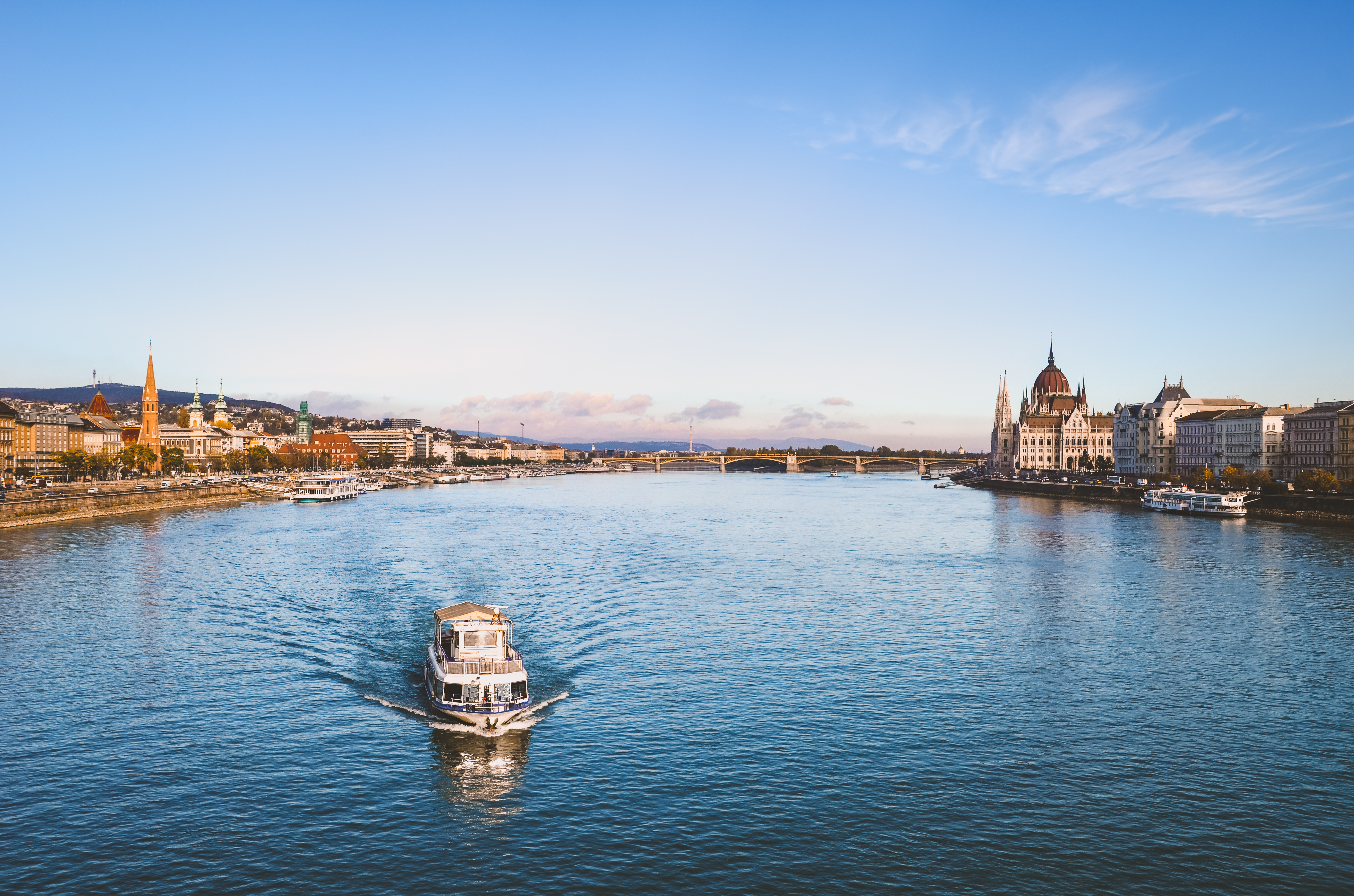 Smuk udsigt over Donaufloden i Budapest med turistbåd og det imponerende ungarske Parlament omgivet af historiske bygninger