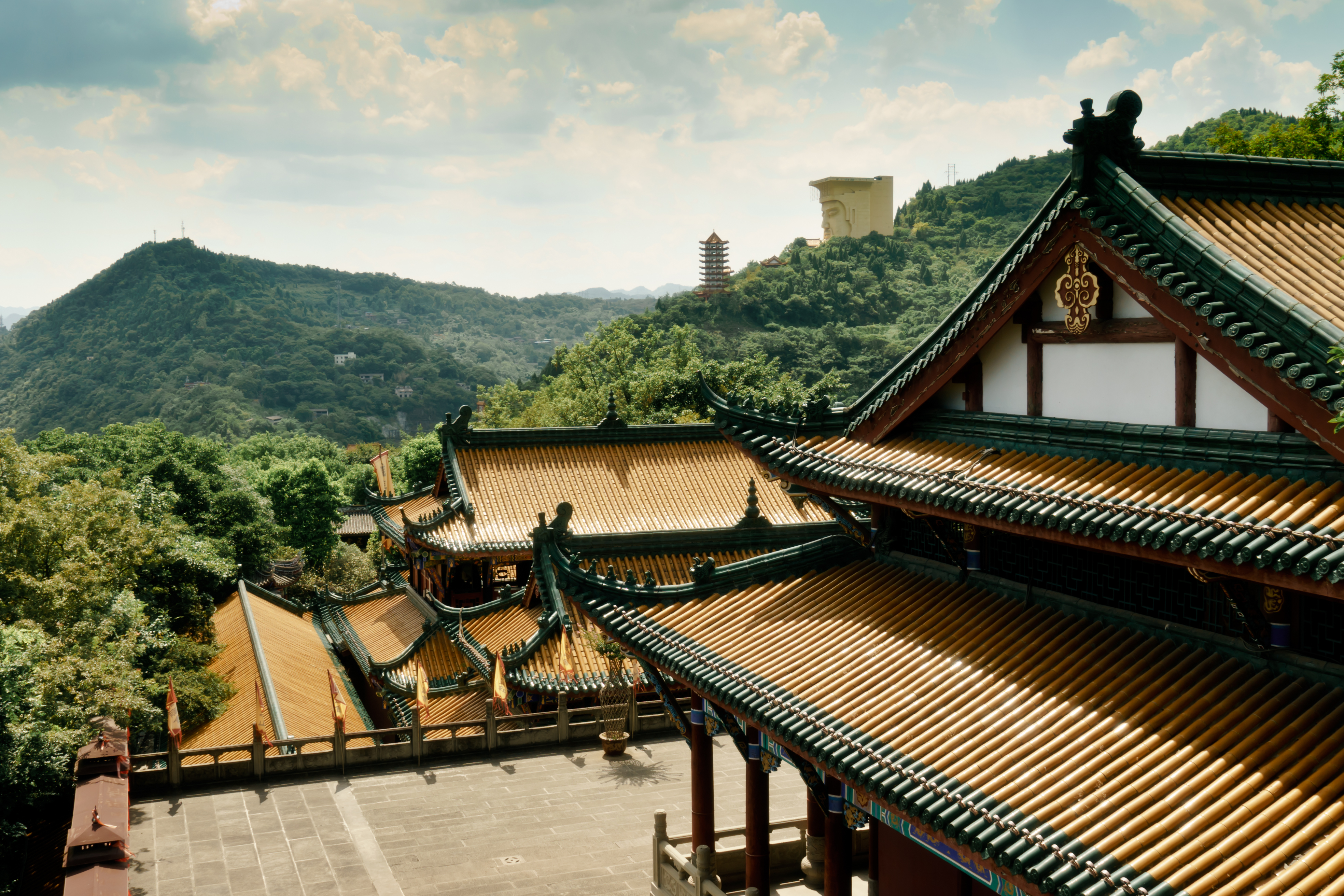 Smukt kinesisk tempelkompleks med gyldne og grønne tagflader set fra oven med en pagode og frodige bjerge i baggrunden ved Yangtze-floden i Chongqing, Kina
