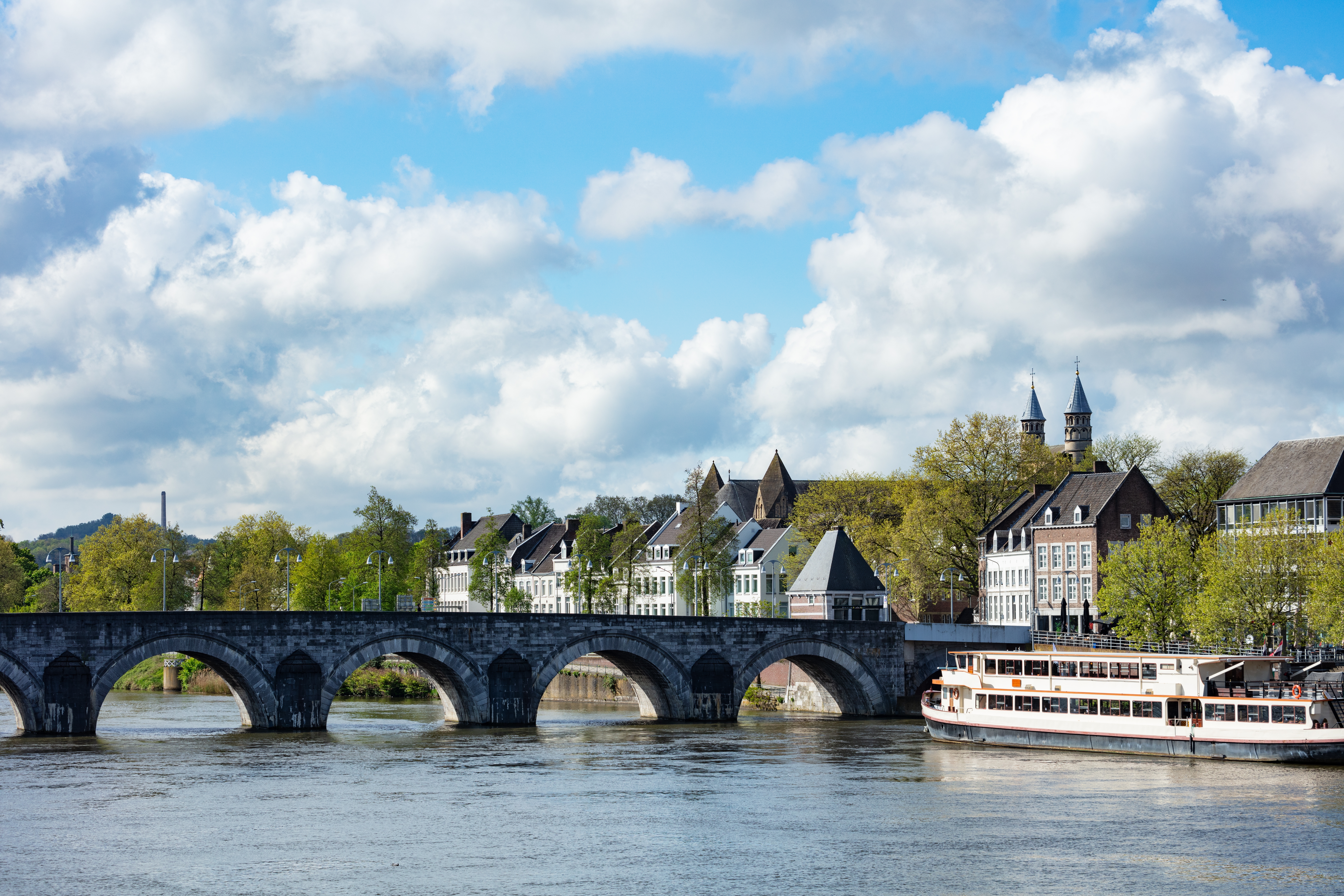 Buebro over flod med sightseeing-båd og kirkelige tårne i baggrunden