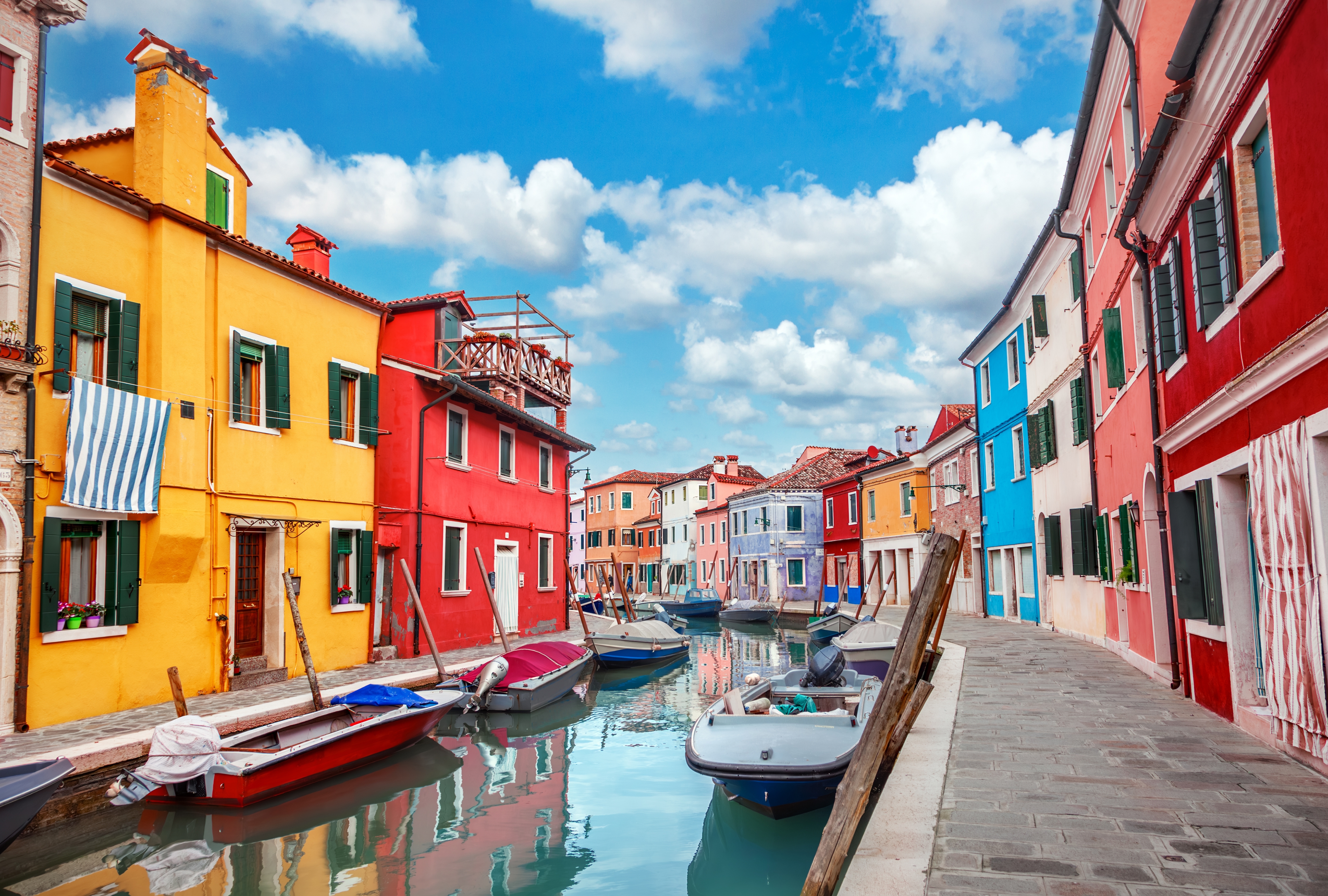 De ikoniske farvestrålende huse på øen Burano ved Venedig med smalle kanaler og traditionelle italienske både på en solrig sommerdag