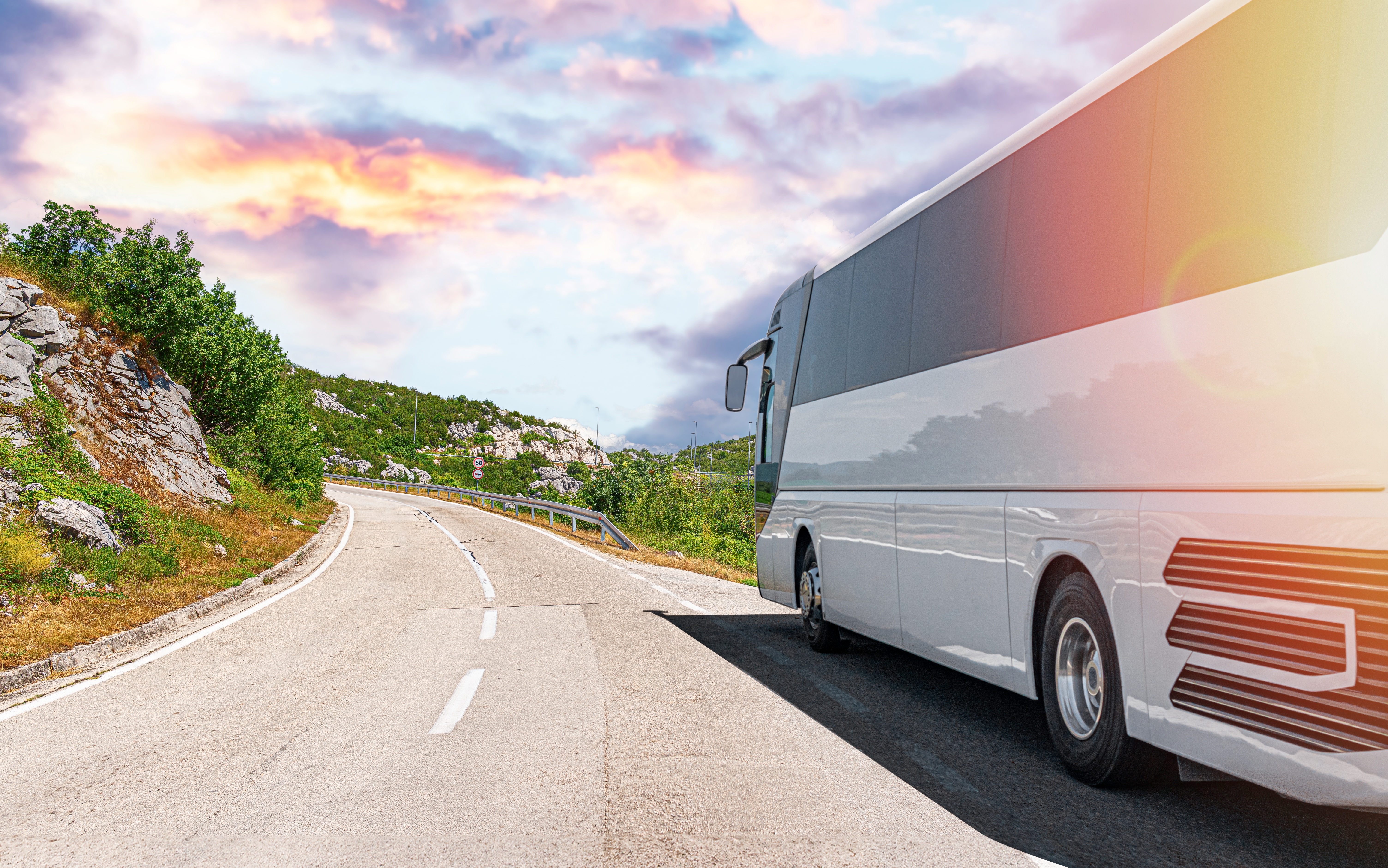 Bus på landevej ved solnedgang under grupperejse i europæiske bjerge