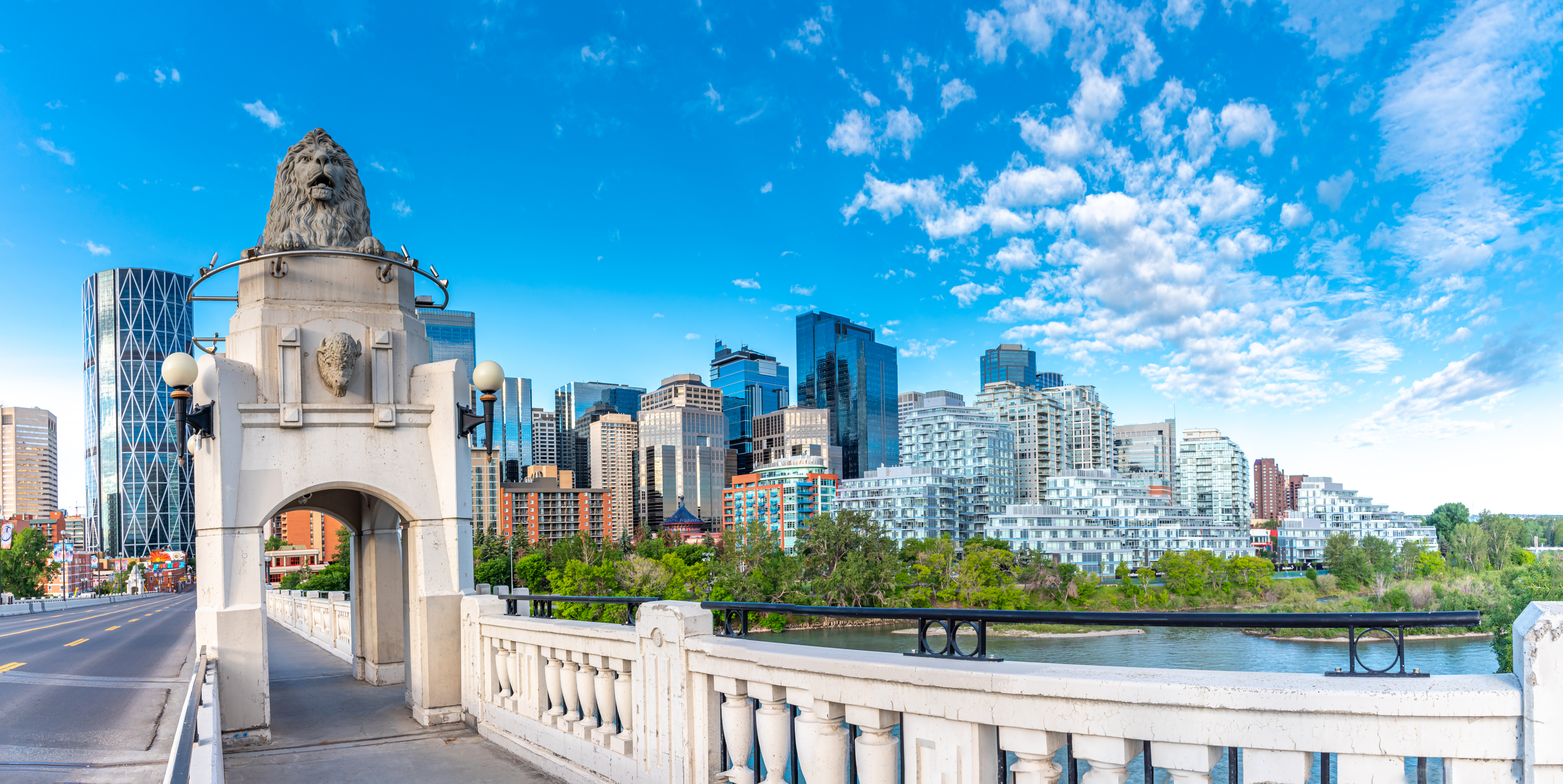 Panoramisk udsigt over Calgarys centrum med den klassiske Centre Street Bridge og moderne skyskrabere spejlet i Bow River på en klar sommerdag