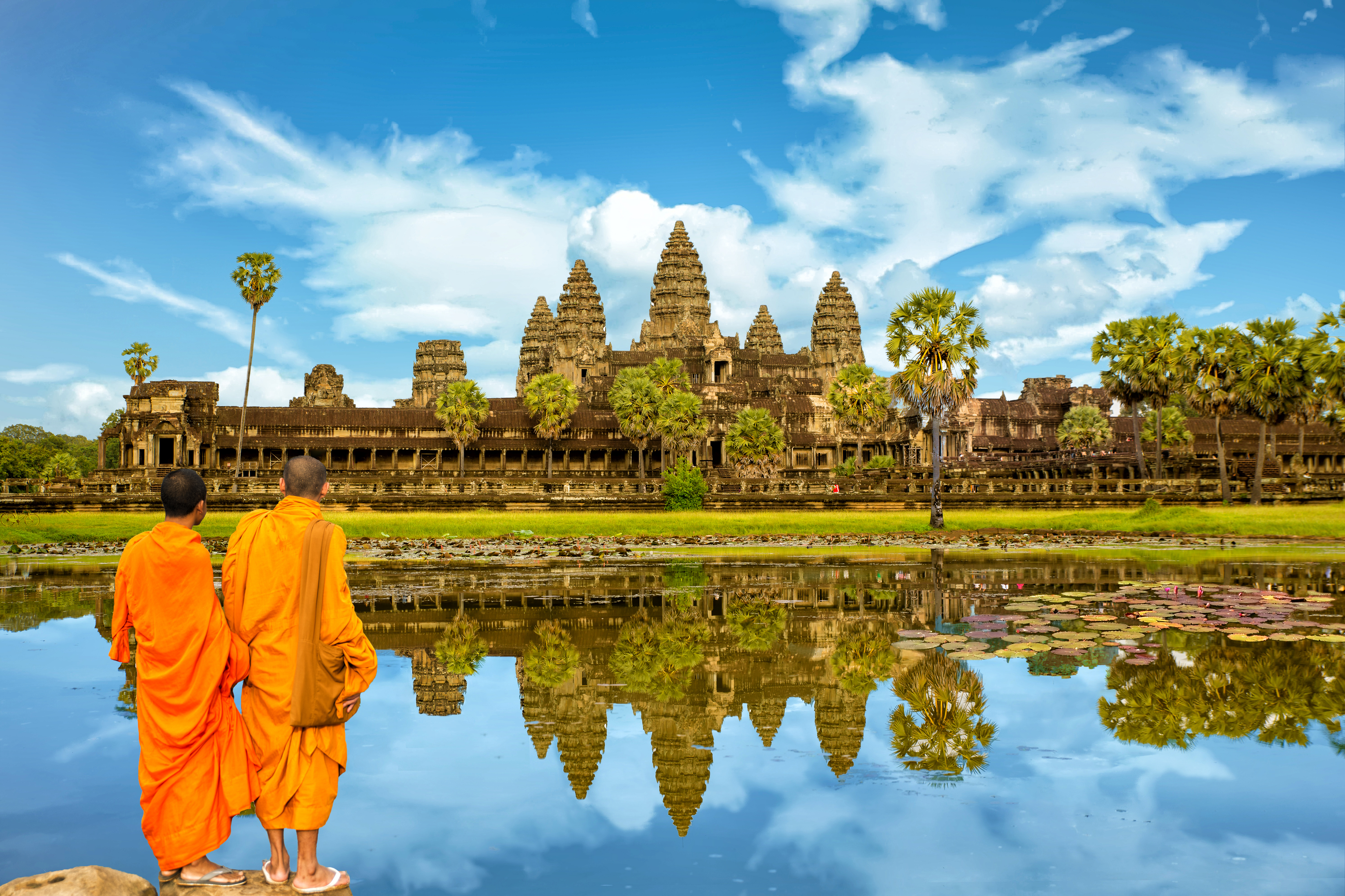 Spektakulaer udsigt til Angkor Wat med buddhistische munke i orange toej ved vandkanten i det tidlige morgenlys