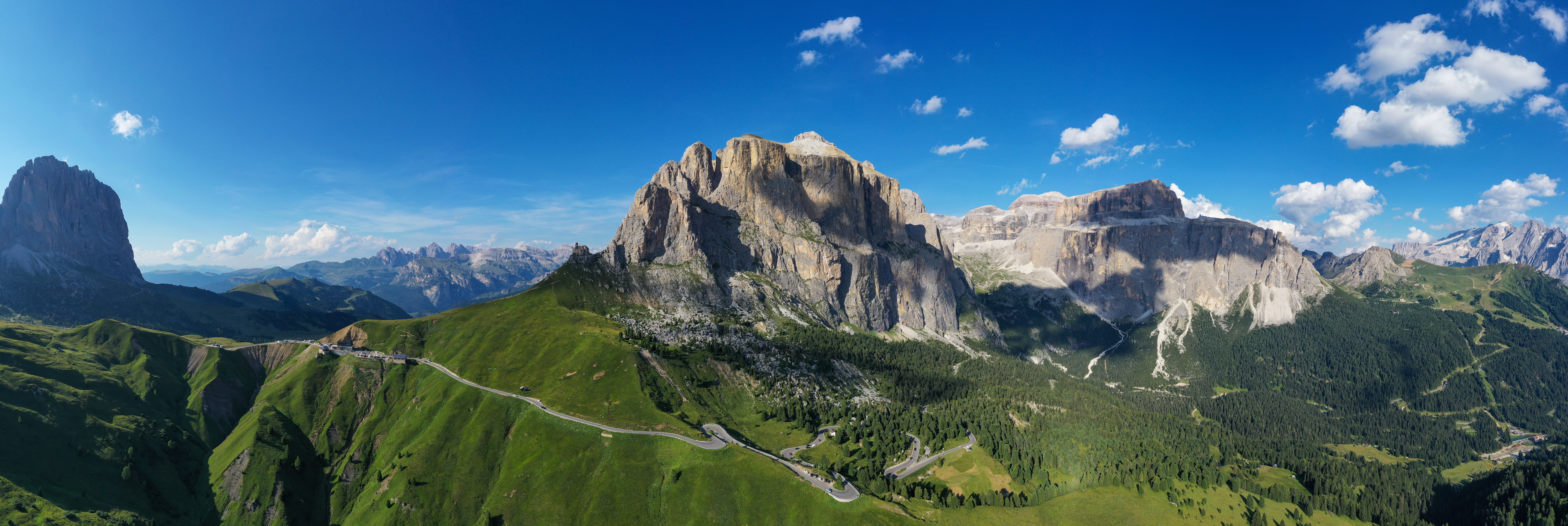 Luftpanorama over Passo Sella og Canazei i Dolomitterne, Italien, med smukke grønne alpelandskaber, imponerende klippevægge og blå sommerhimmel