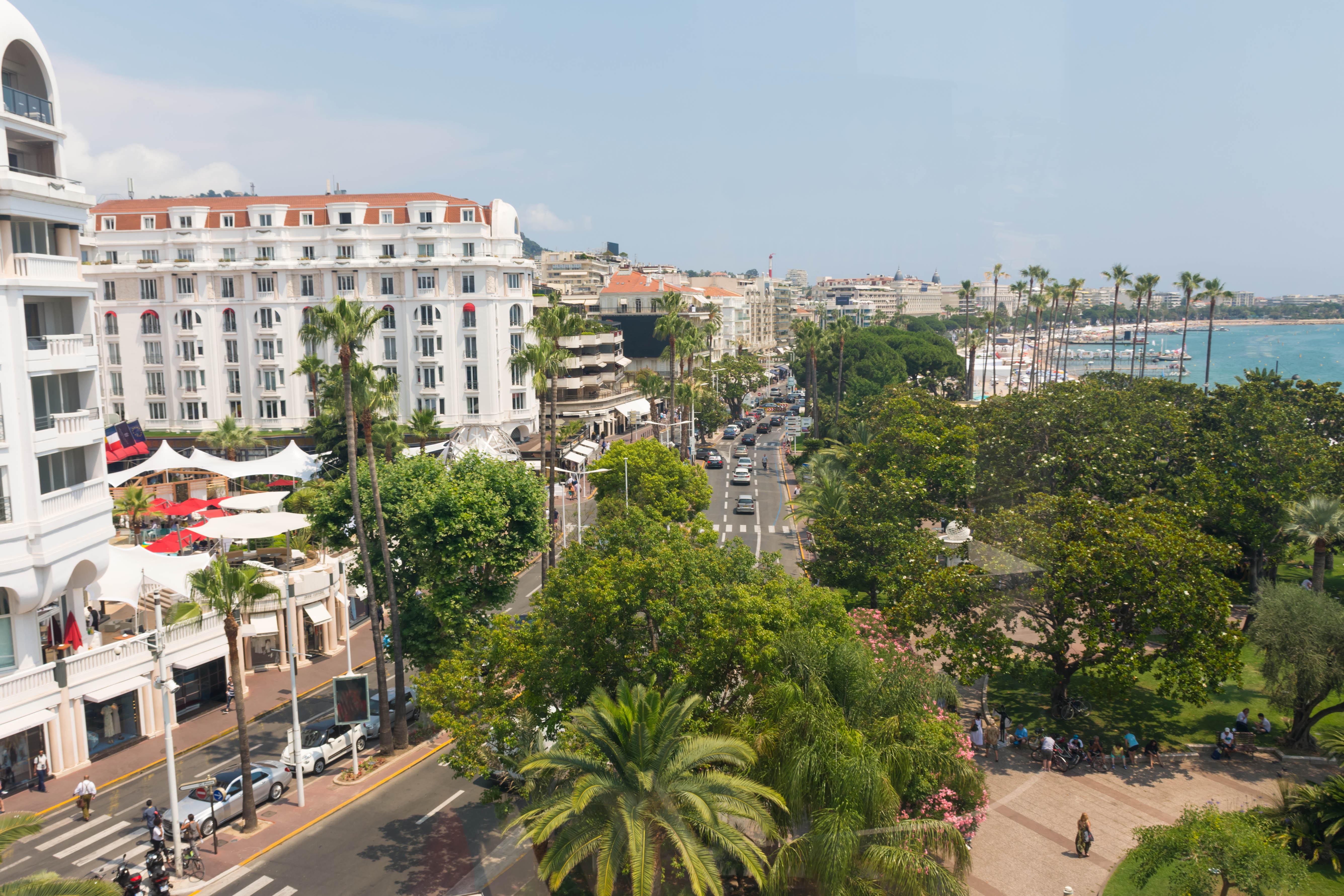 Udsigt over Cannes Boulevard de la Croisette med luksuriøse hoteller, grønne palmetræer og det turkisblå Middelhav
