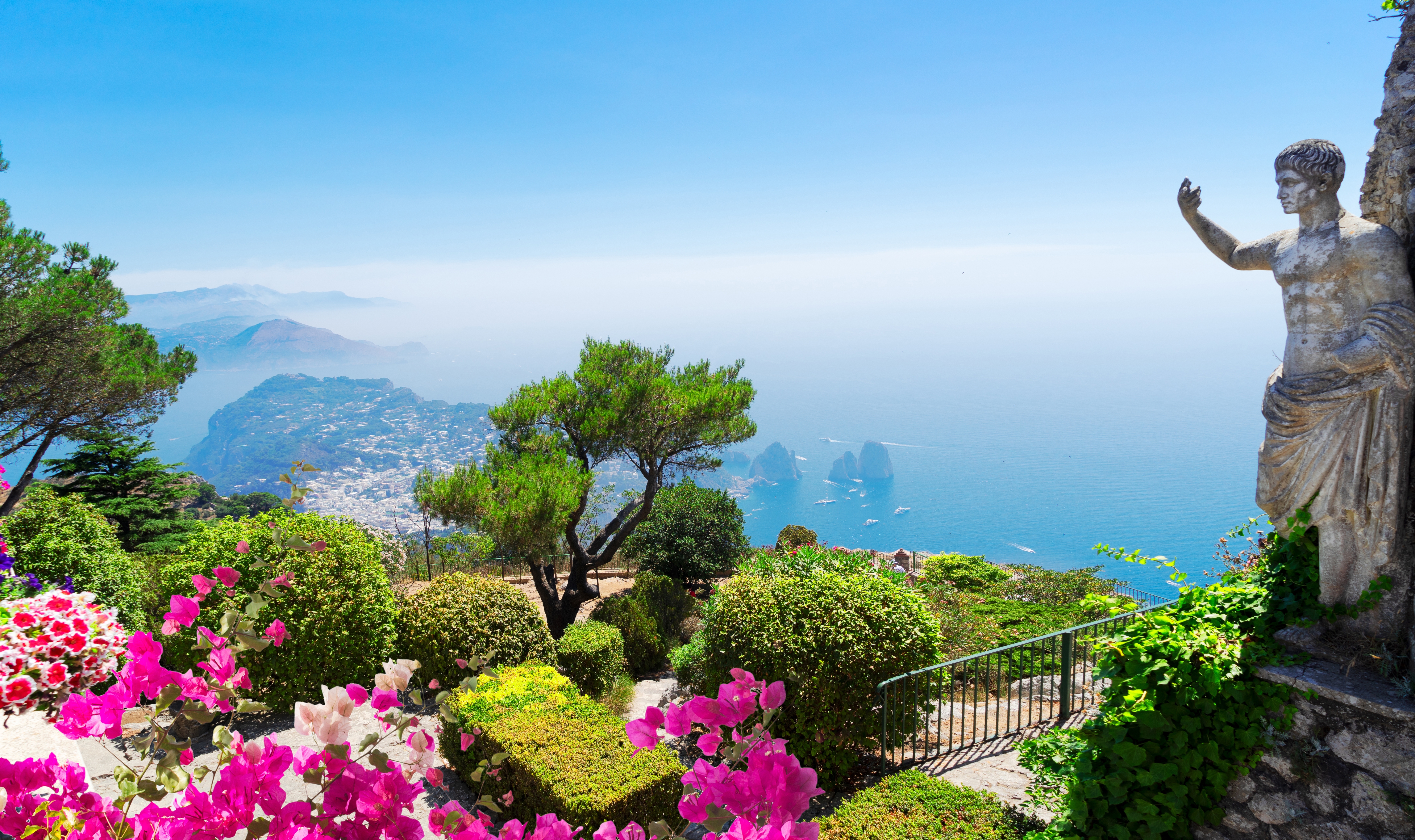 Spektakulær udsigt over Capri med farverige blomster og klassisk statue ved Middelhavet