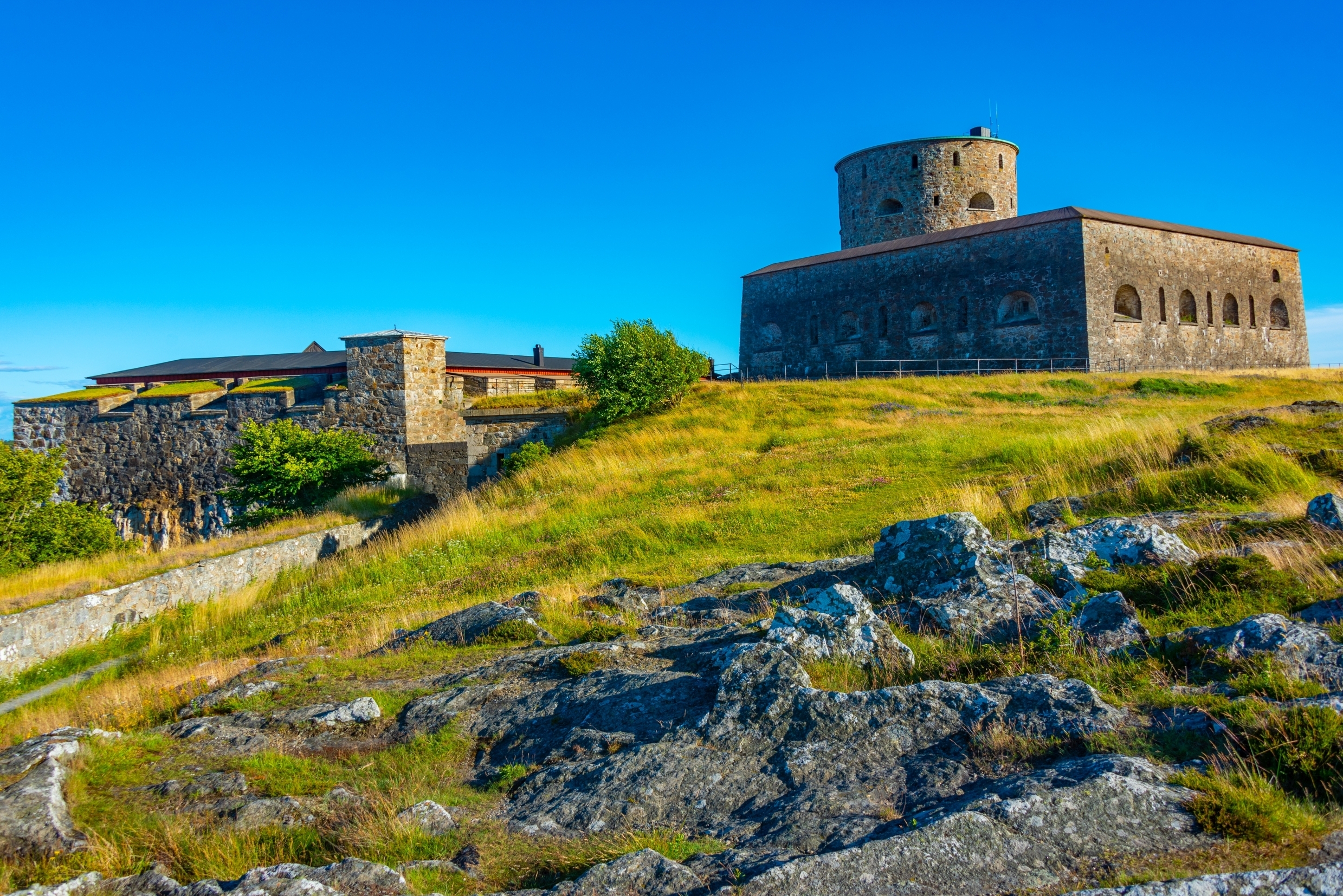 Smukt udsyn til Carlsten Fæstning i Marstrand, Sverige, med historiske stenbyggerier og tårn omgivet af grønt græs og blå himmel
