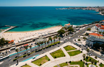 Panoramaudsigt fra luften over Cascais og Estoril-kysten med den indbydende Tamariz Strand, turkist hav og palmeboulevard i Portugal