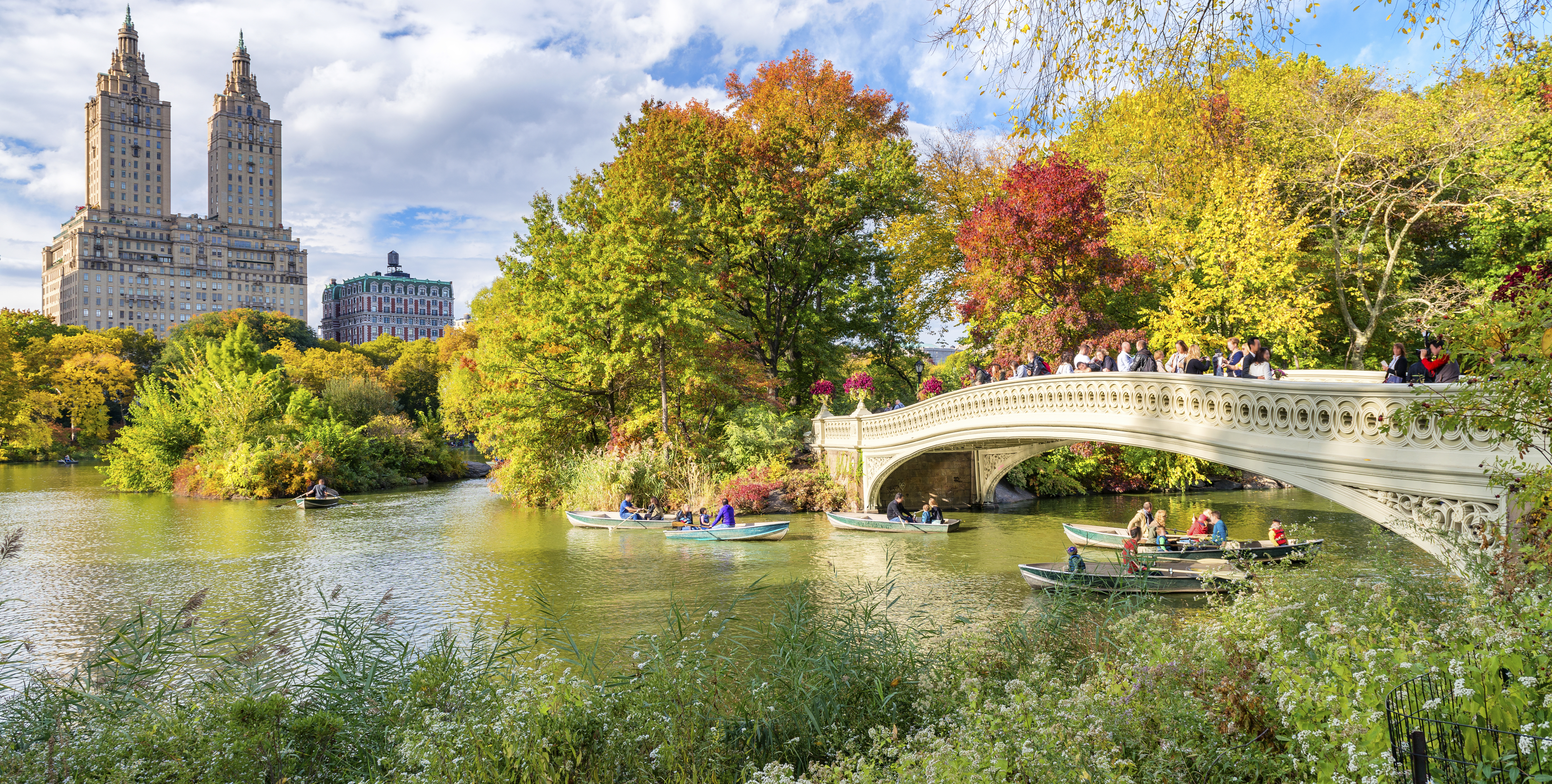 Farverigt efterårslandskab i Central Park med gyldenbrune træer og spejlblank sø - en spektakulær naturoplevelse i hjertet af New York med byens skyline i baggrunden