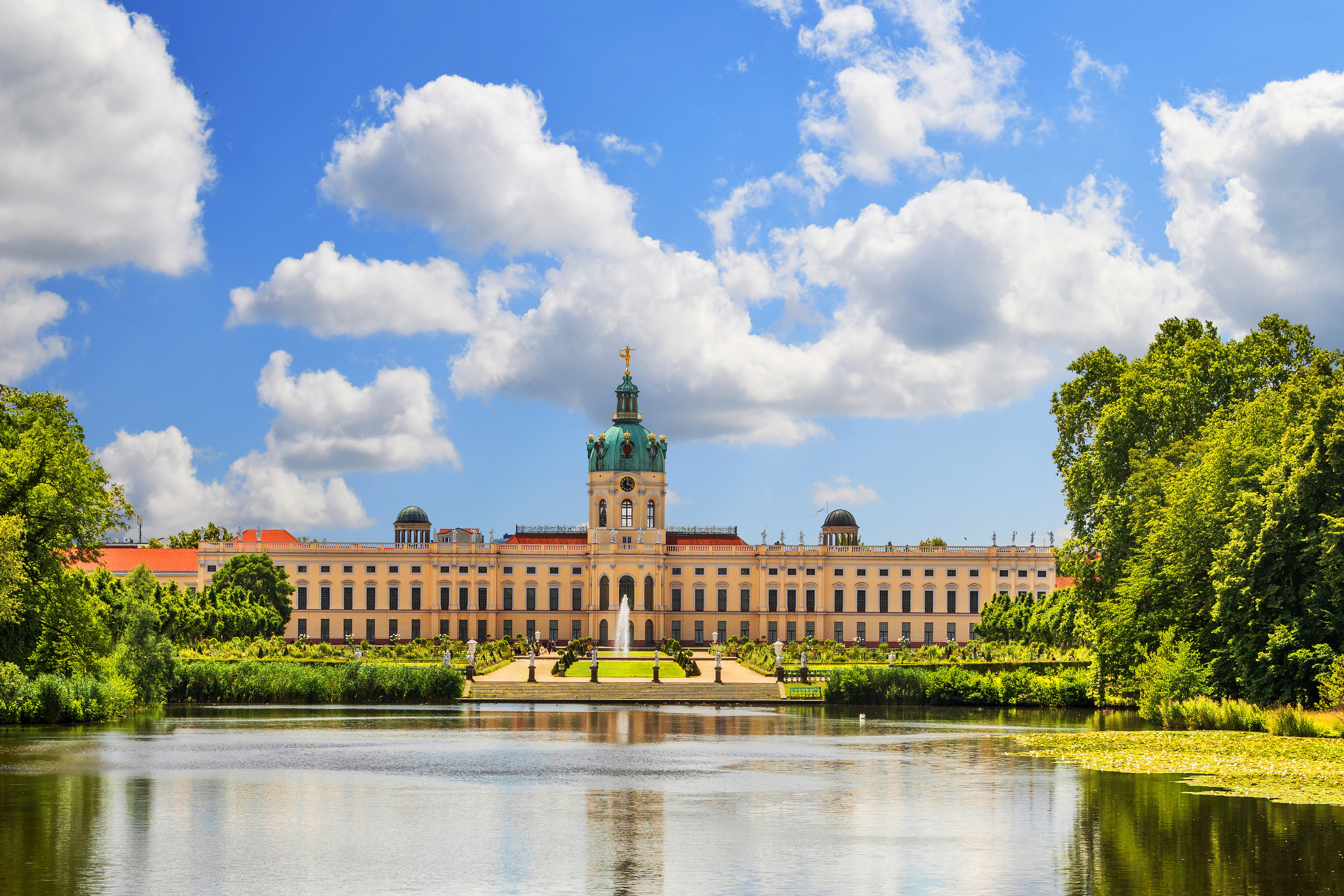 Majestætisk udsigt over Charlottenburg Slot i Berlin med barok facade, grøn kuppel, velplejet slotshave, springvand og rolig sø på en skyfri sommerdag