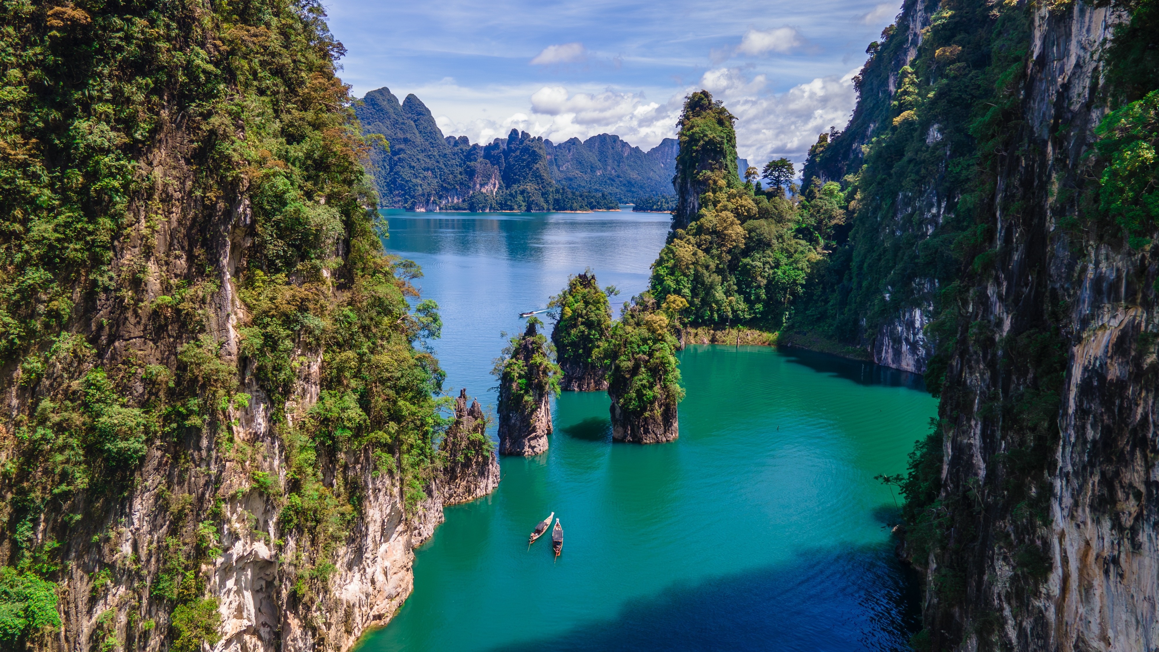Longtailbåd på det turkisblå Cheow Lan vand omgivet af kalkstensklinter i Khao Sok Nationalpark, Thailand