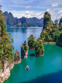 Longtailbåd på det turkisblå Cheow Lan vand omgivet af kalkstensklinter i Khao Sok Nationalpark, Thailand