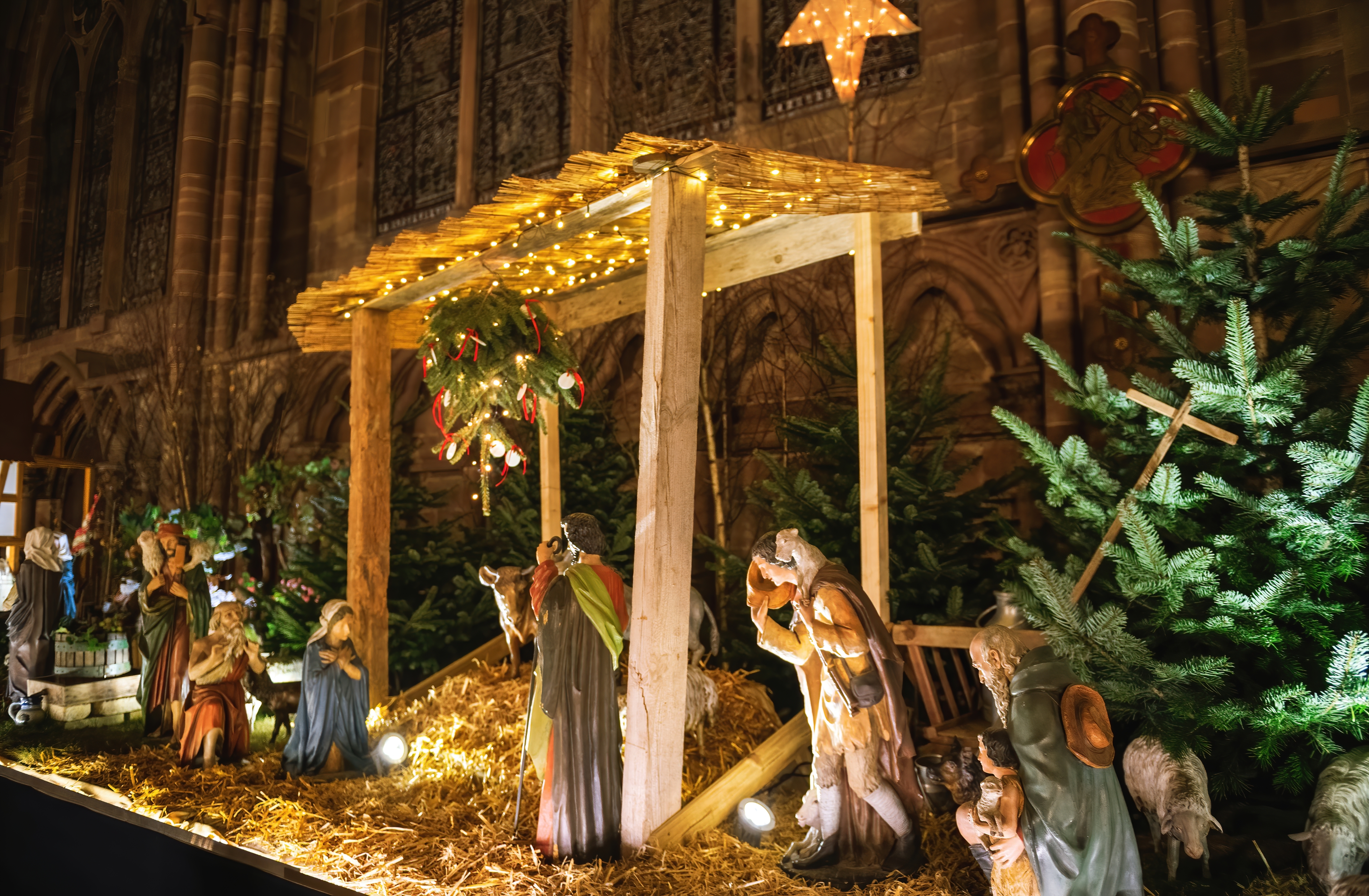 Autentisk julekrybbe ved europæisk domkirke med Maria, Josef og Jesusbarnet omgivet af varmt lys og julepynt