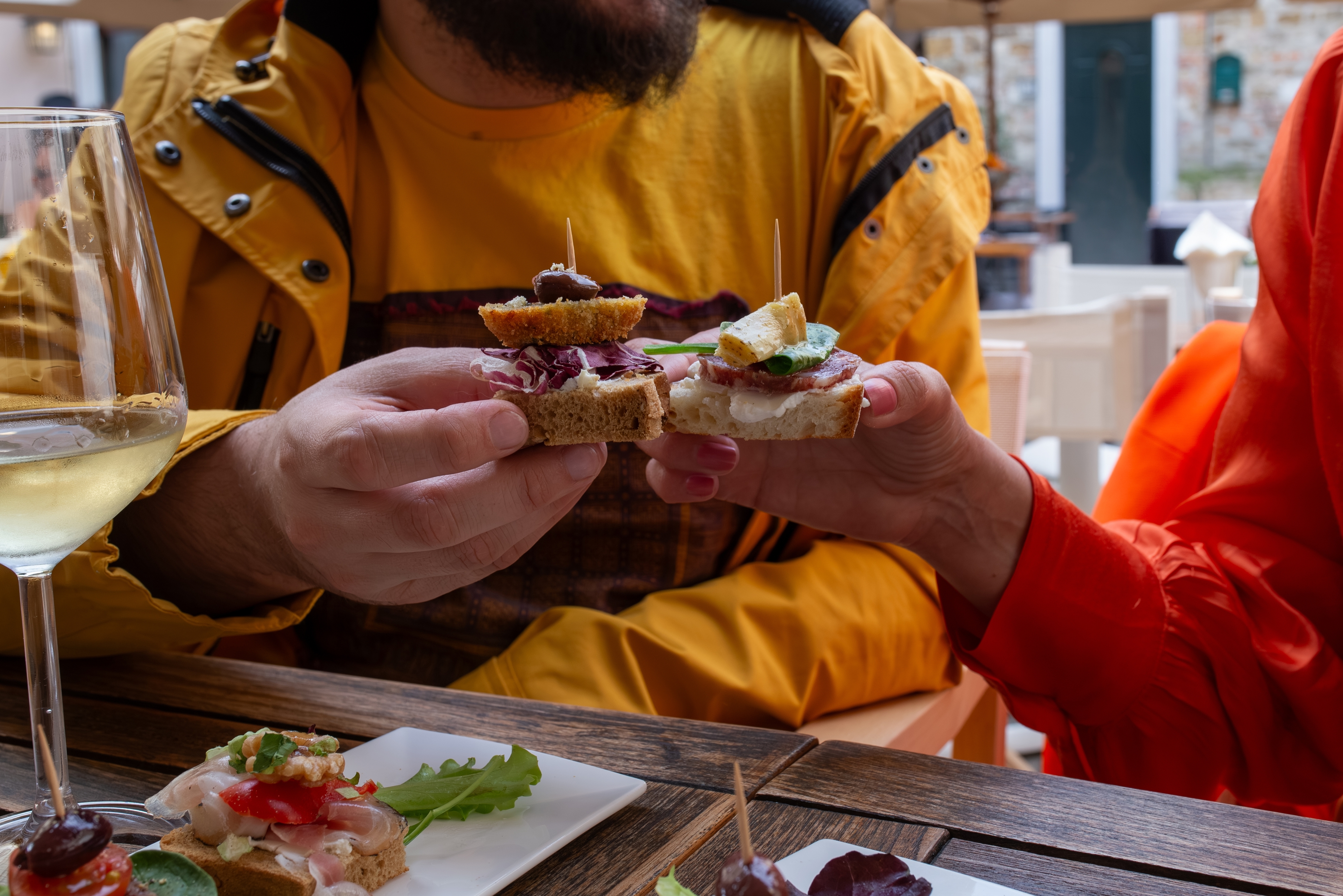 To personer fejrer det italienske aperitivo-ritual med et skål af crostini og cicchetti, omgivet af hvidvin og snacks