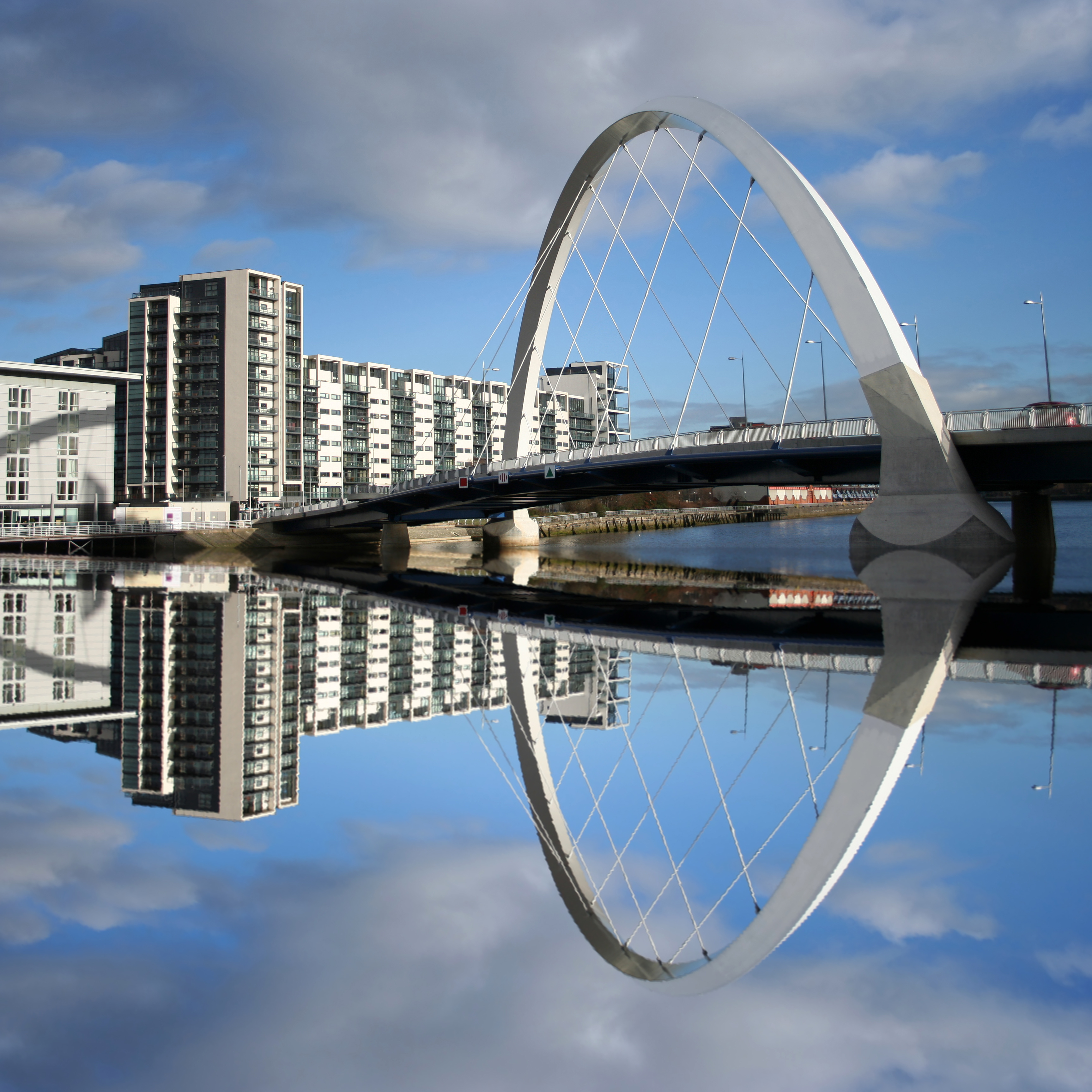 Clyde Arc-broen i Glasgow, Skotland, spejler sig smukt i River Clyde med moderne bygninger langs bredden