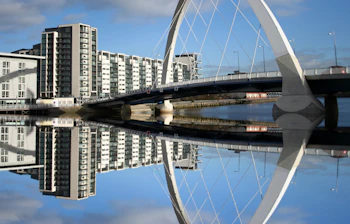Clyde Arc-broen i Glasgow, Skotland, spejler sig smukt i River Clyde med moderne bygninger langs bredden