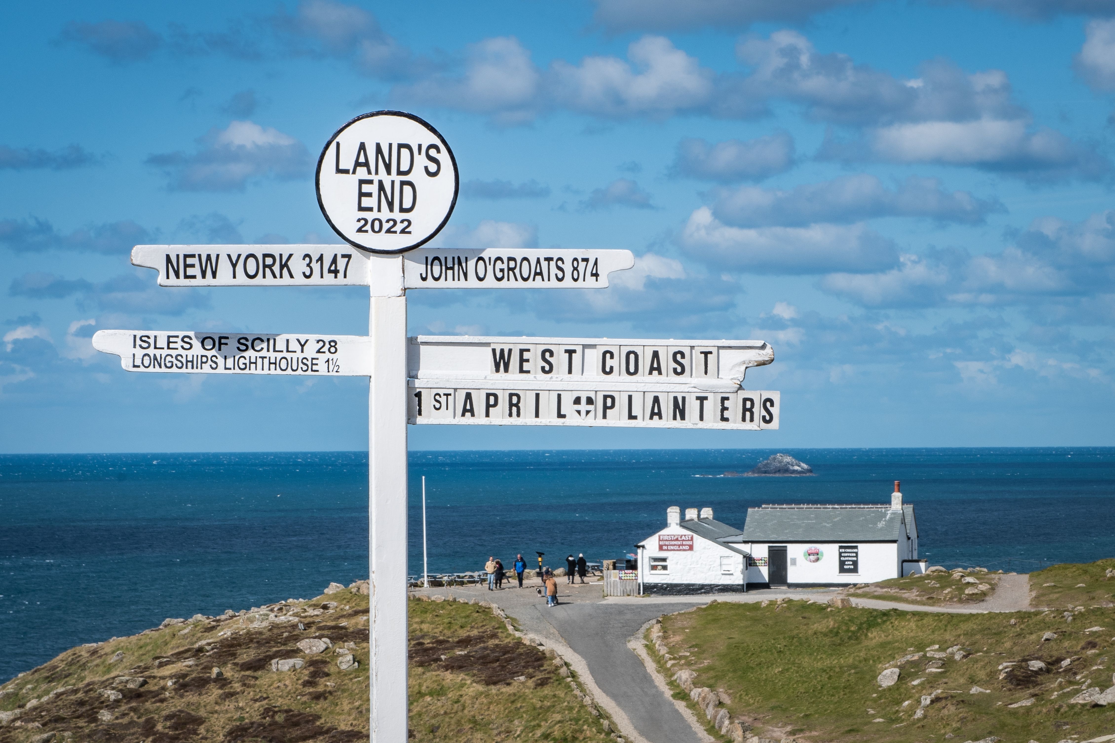 Traditionel retningsviser ved Lands End med skilte til New York og John O'Groats med den imponerende atlanterhavskyst i baggrunden