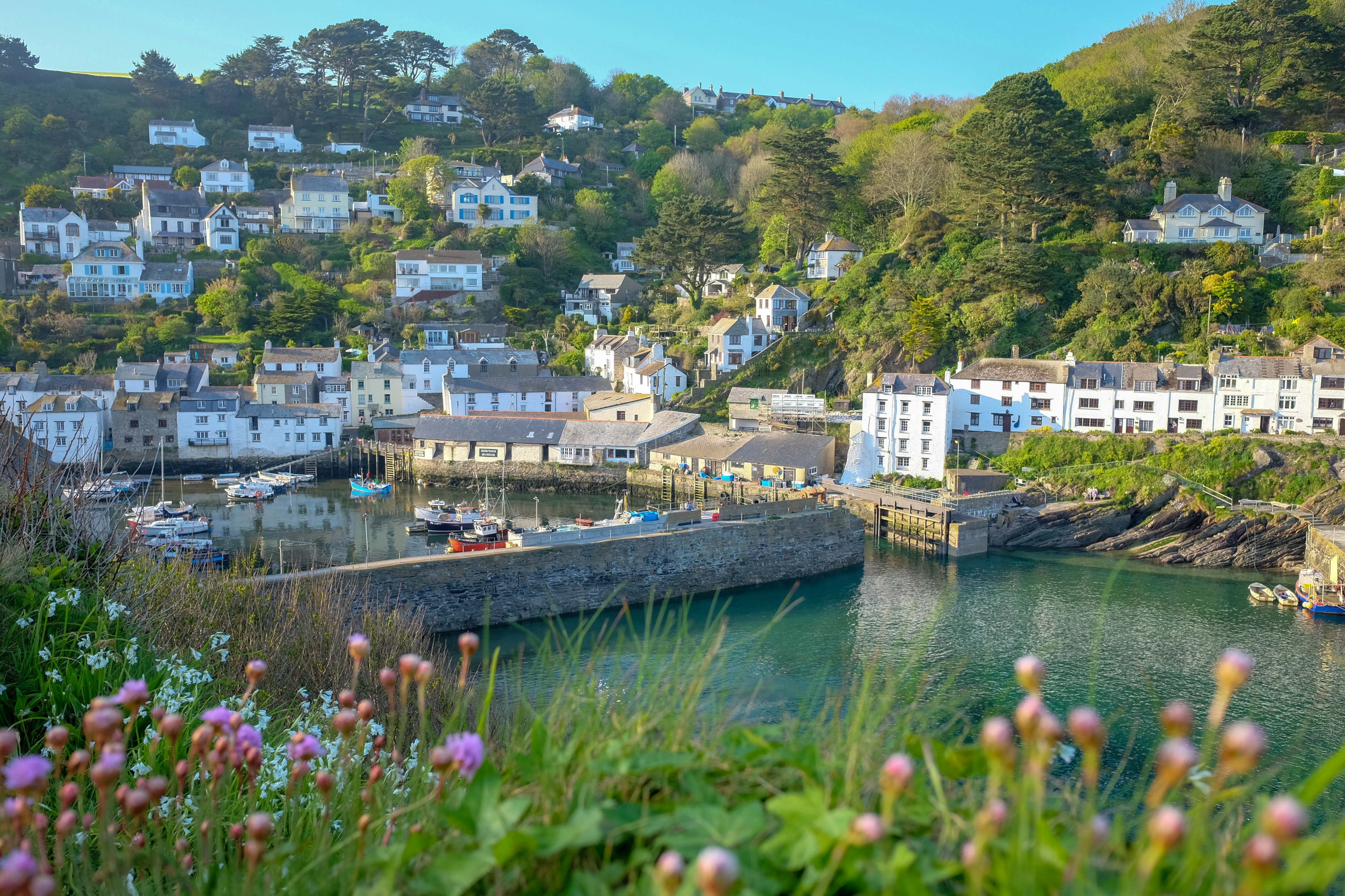 Cornwall kystby med beskyttet havn, forankrede både og karakteristiske hvide huse bygget på den grønne bakke