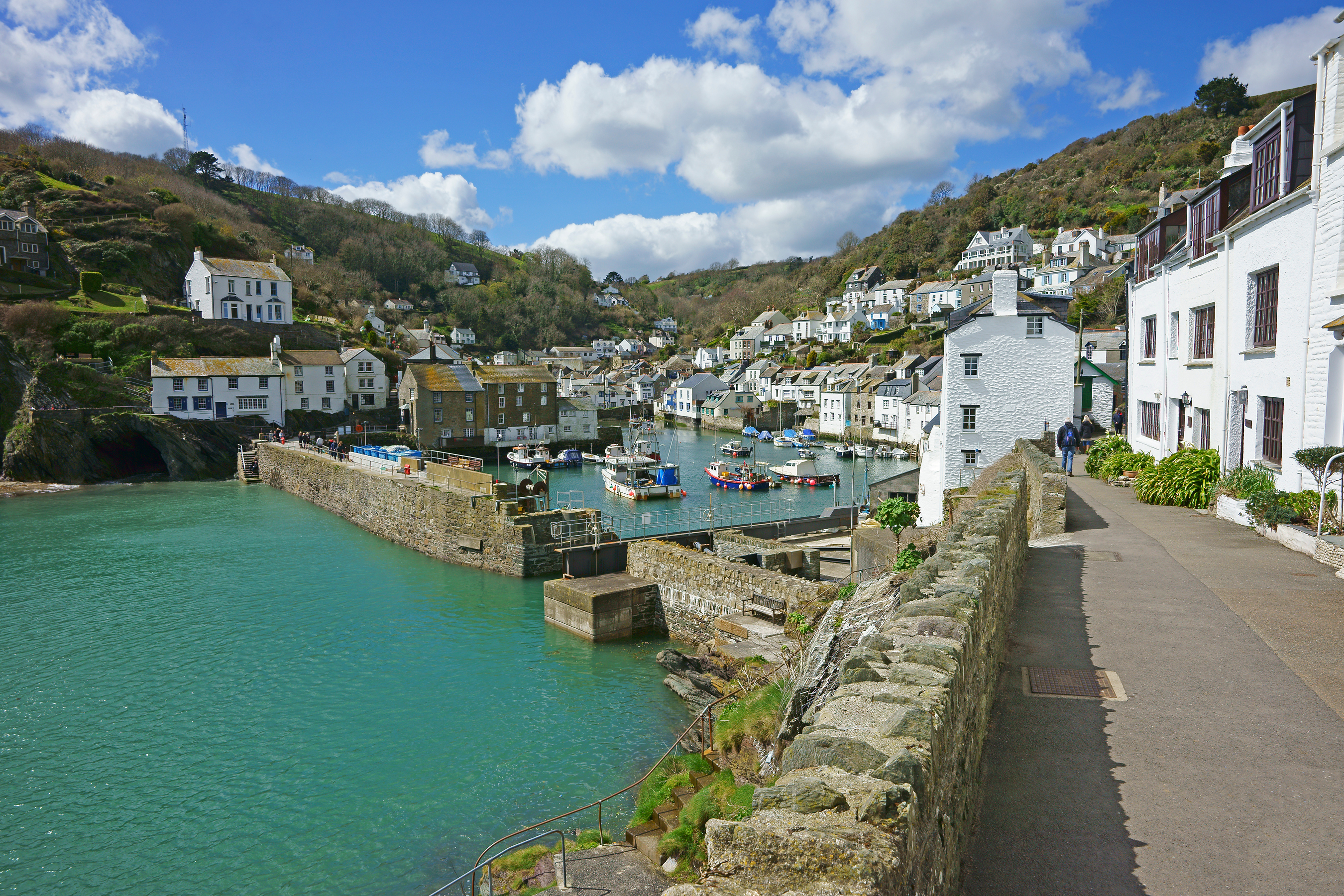 Hyggelig engelsk kystby Polperro i Cornwall med den smukke naturhavn, hvide huse langs kajkanten og grønne bakker under blå himmel