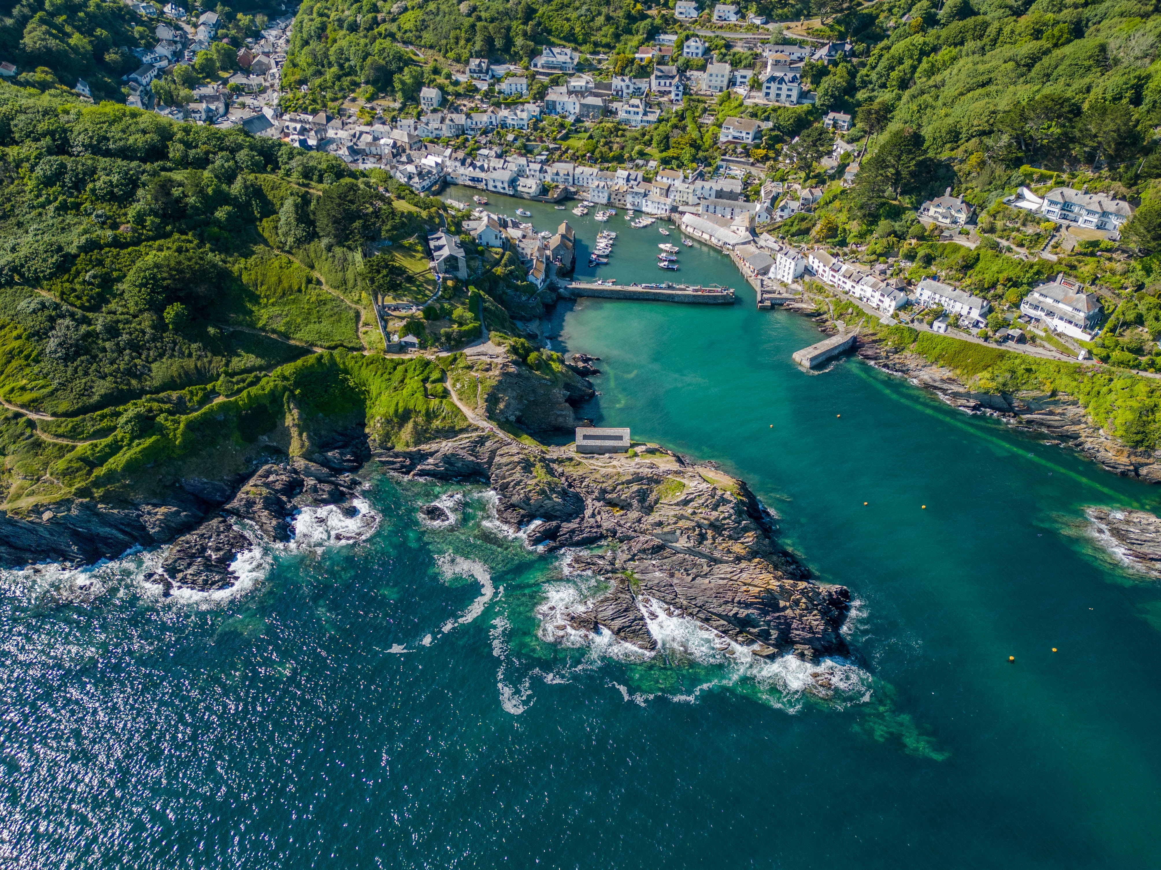 Smukt luftfoto af kystbyen Polperro i Cornwall, England, med idyllisk havn, turkisblåt vand og grønne klippeskrænter