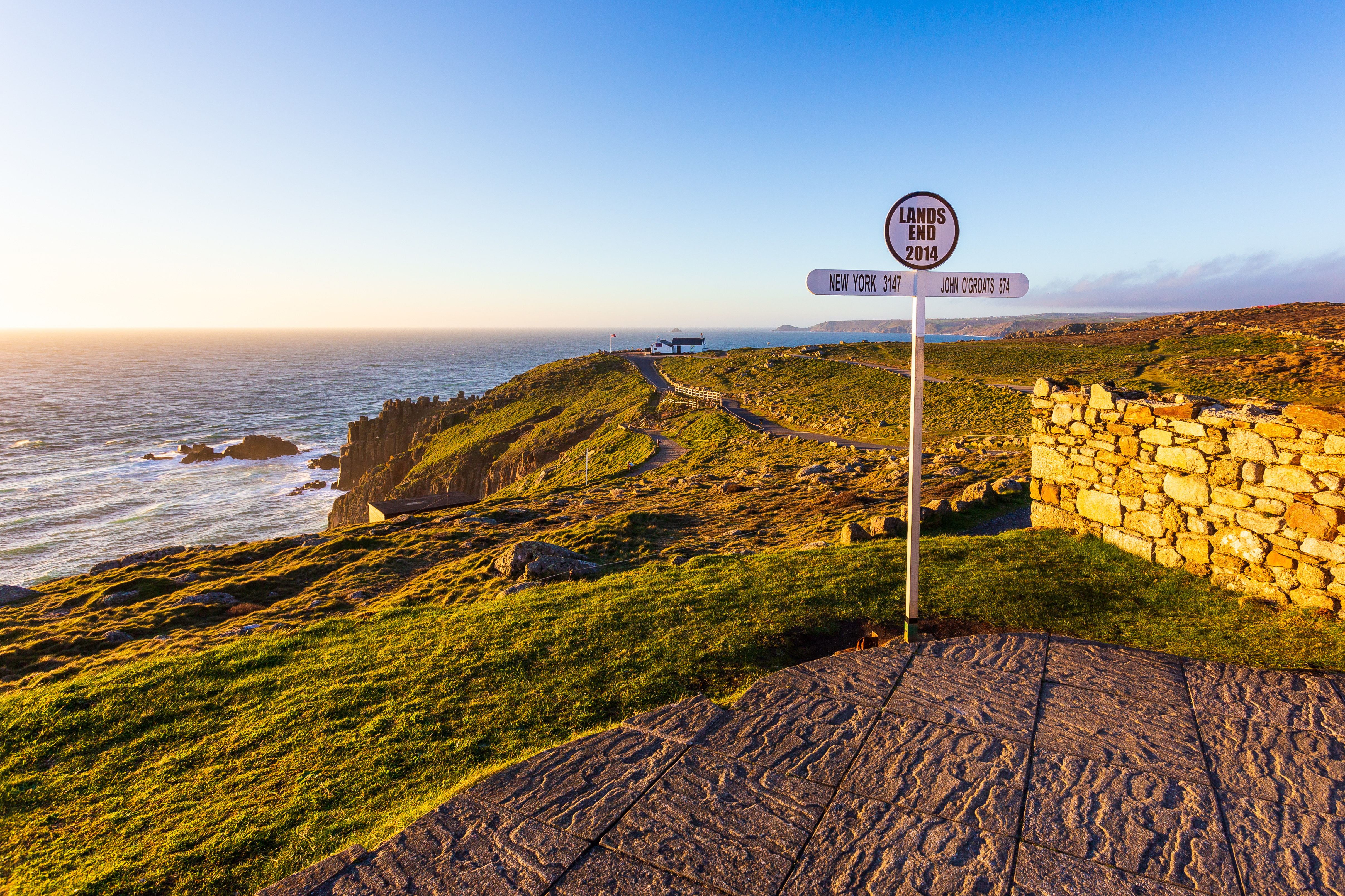 Vejviser ved Englands vestligste punkt Lands End i Cornwall med gylden solnedgang over klippekysten