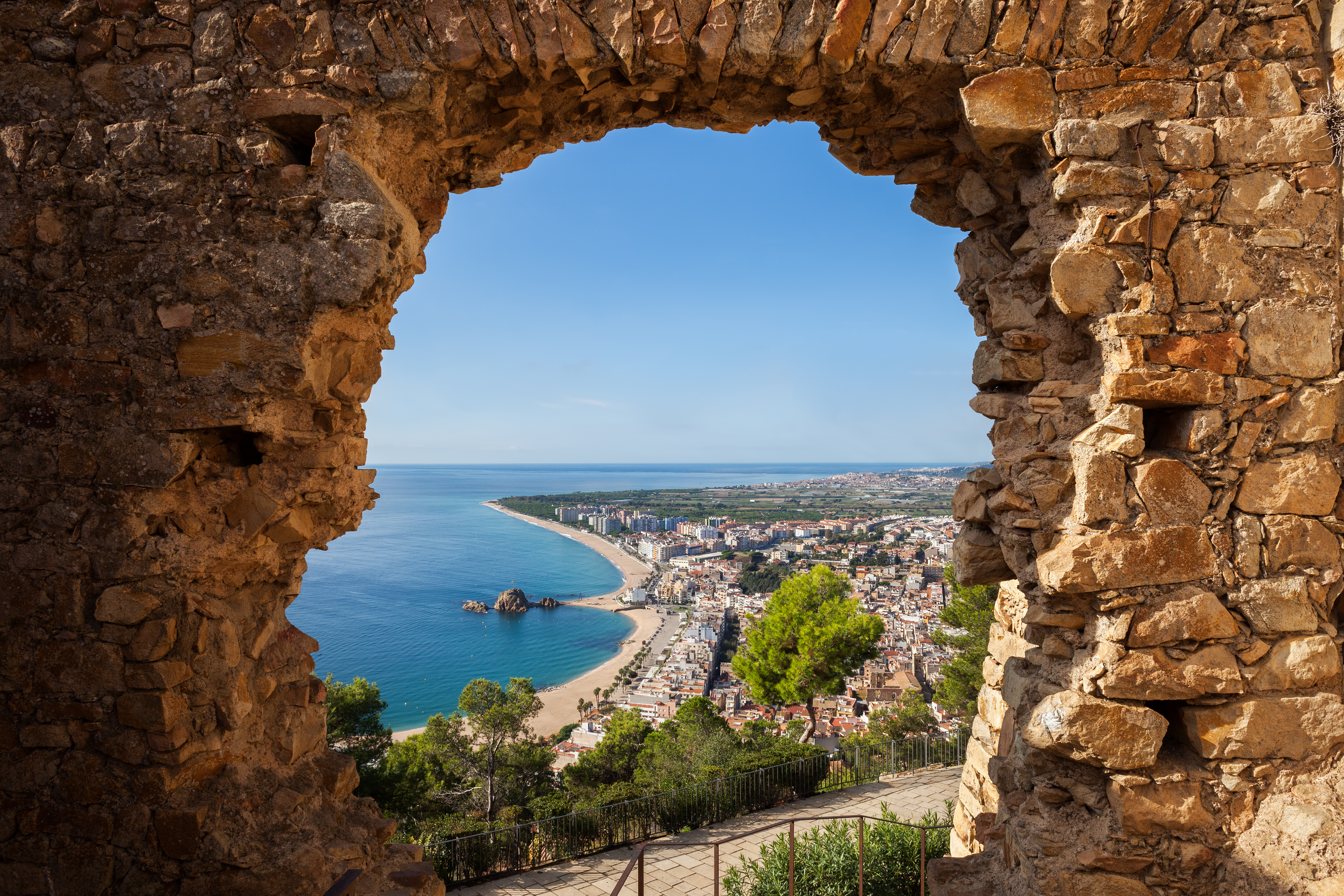 Malerisk panorama over feriebyen Blanes ved Costa Brava, indrammet af en åbning i den gamle St. John slotsruin