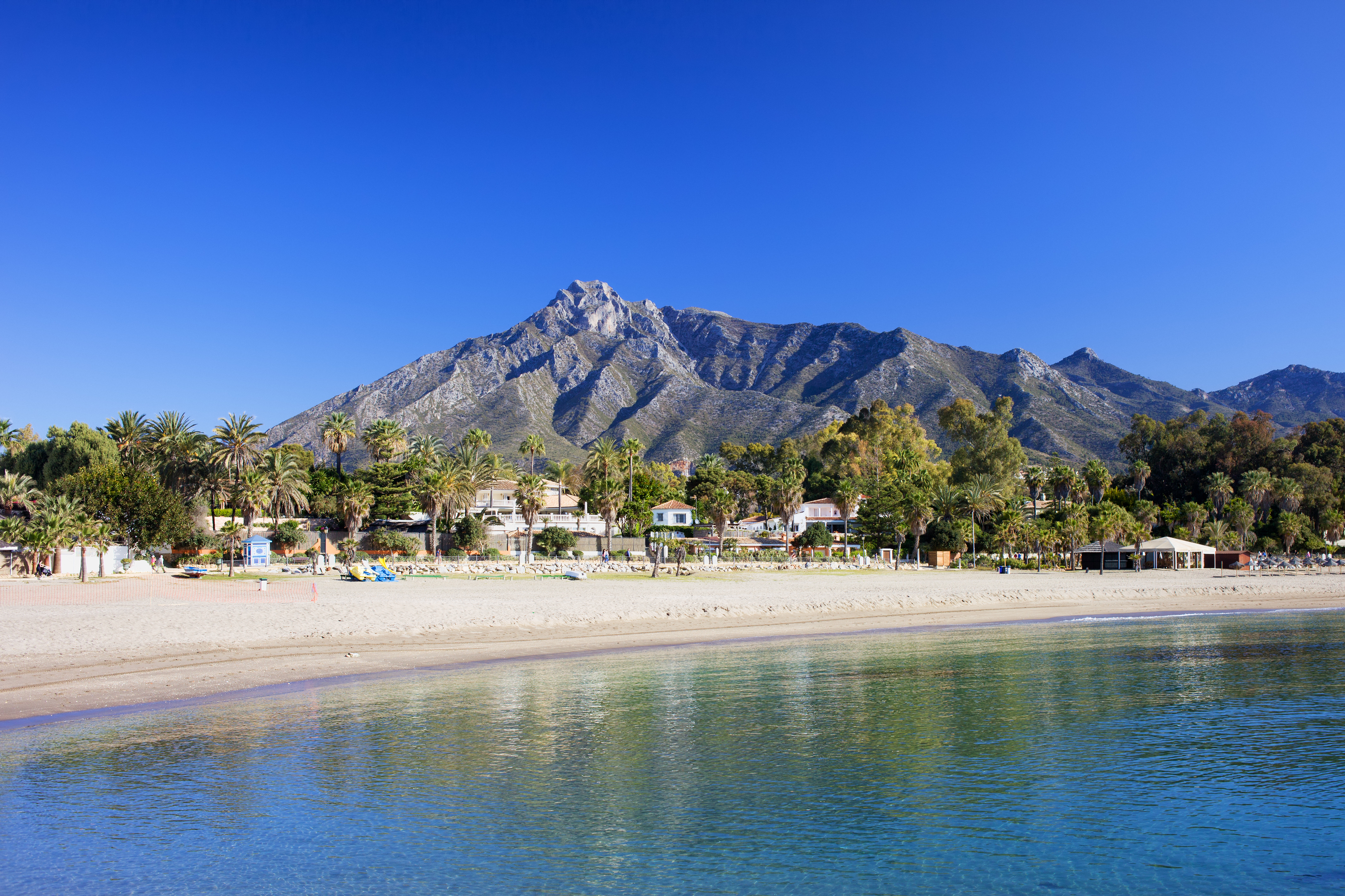 Idyllisk feriestrand i Costa del Sol Marbella med turkisblåt vand og bjergkæde