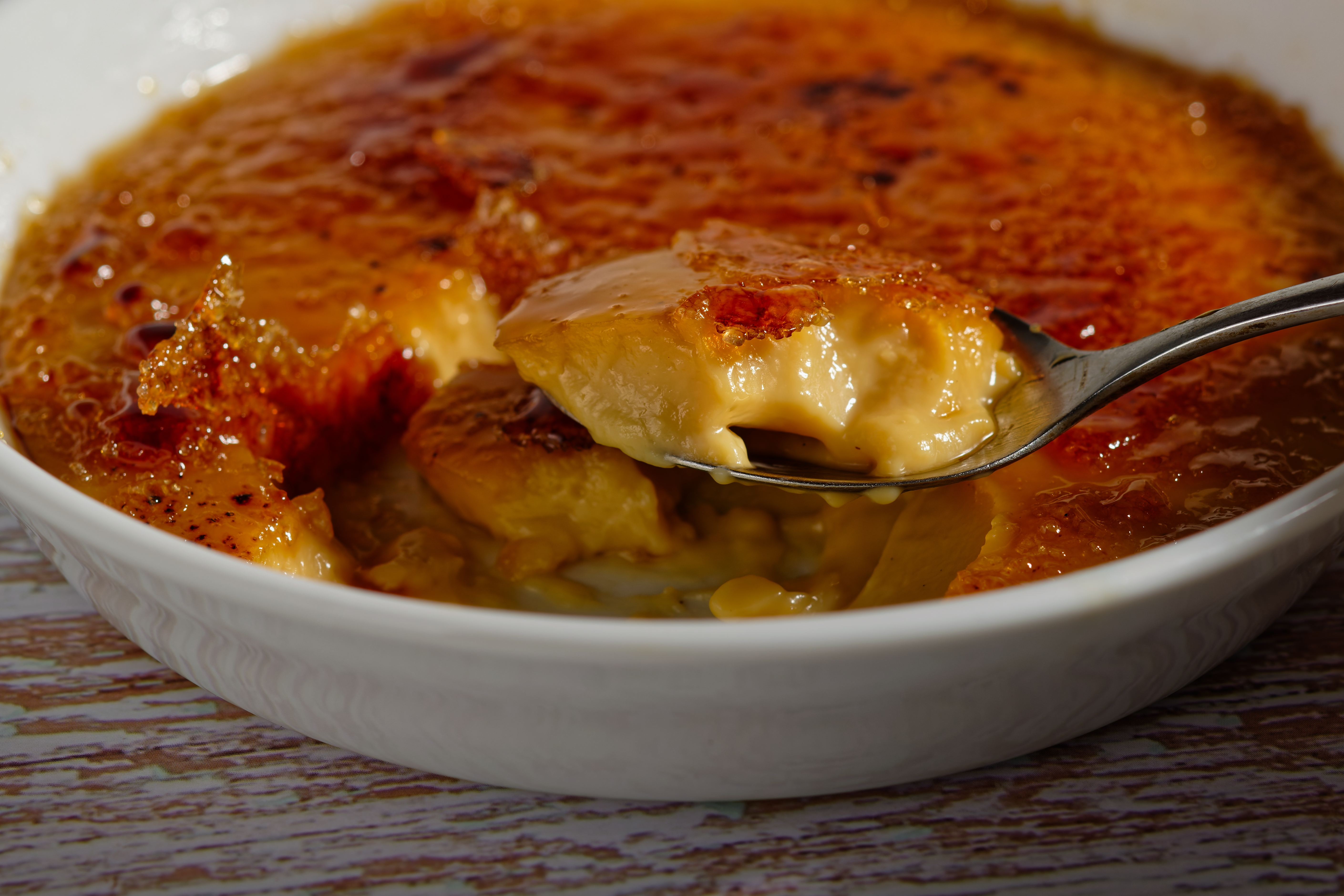 Nært billede af autentisk fransk crème brûlée med sprød karameliseret overflade og blød creme, serveret i hvid ramekin